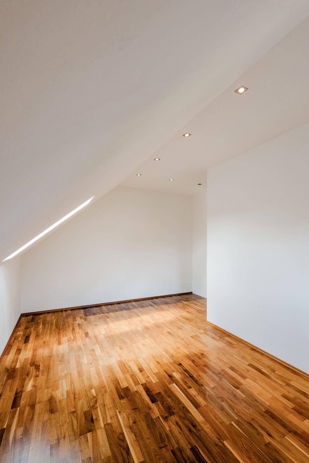 Lichtdurchfluteter Raum mit Holzboden und schräger Decke mit Fenster.