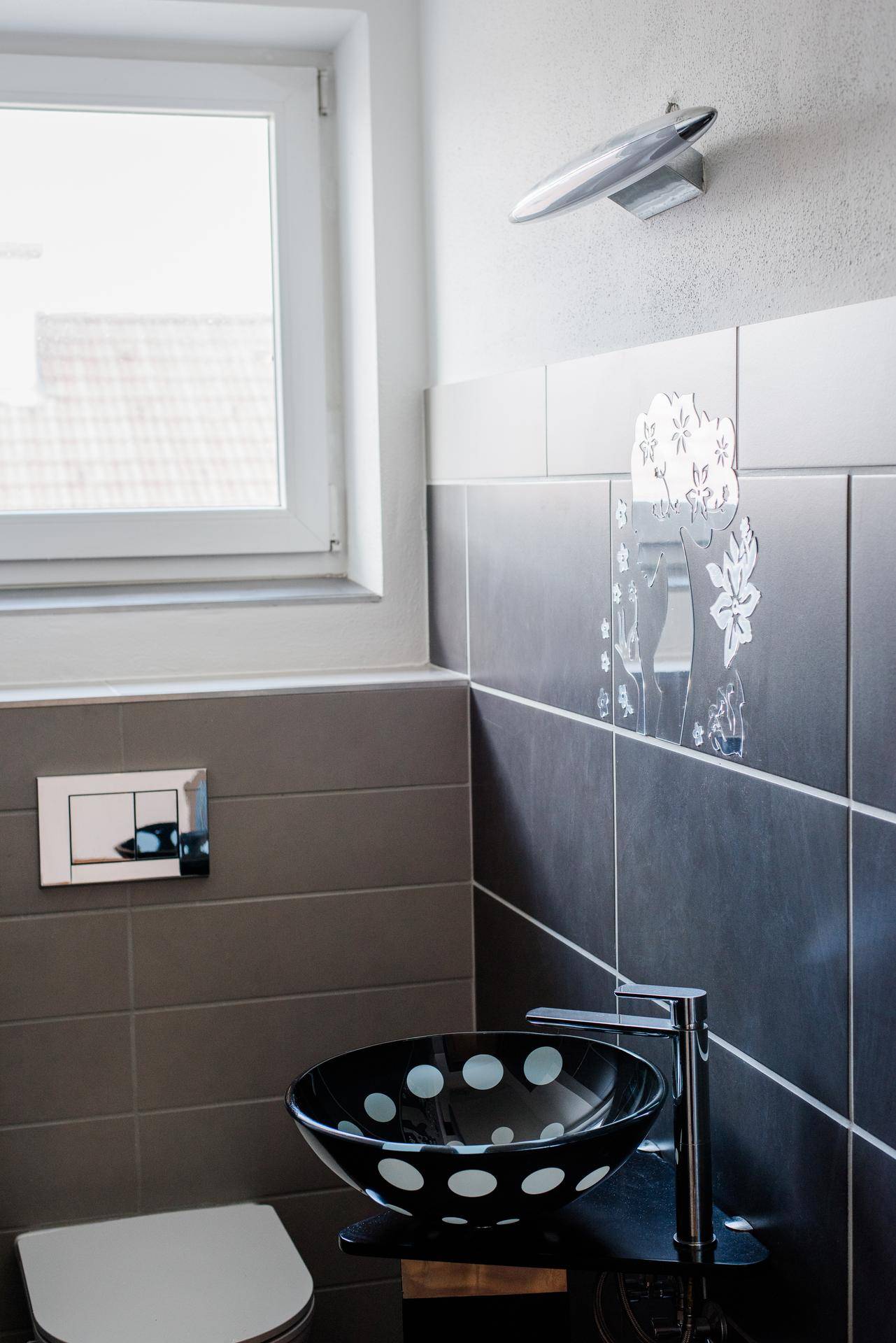 Gäste-WC mit auffälligem schwarzen Waschbecken und Fenster für Tageslicht.