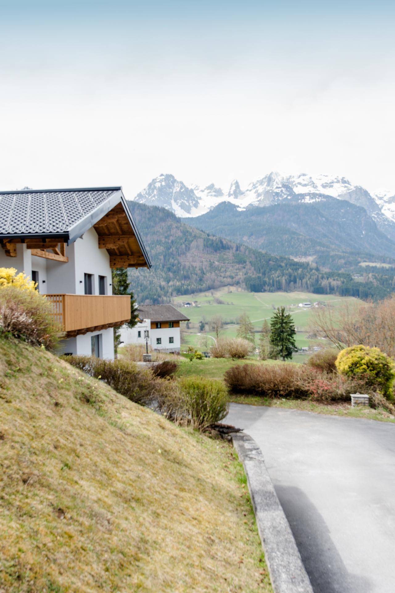 Modernes Haus am Hang mit Holzbalkon und beeindruckendem Blick auf die Alpen.