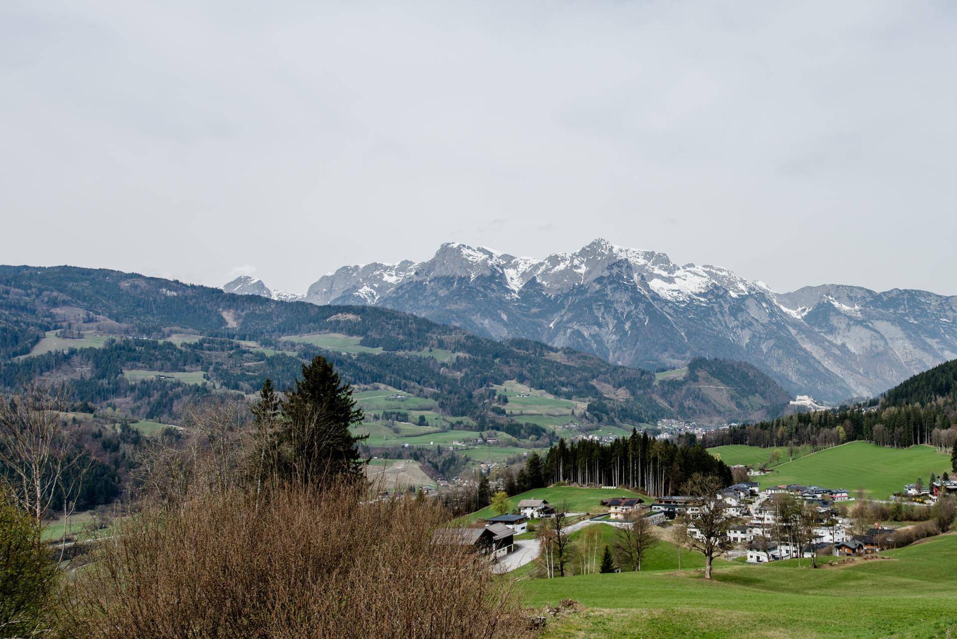 Panoramablick auf eine malerische Alpenlandschaft mit grünen Tälern und schneebedeckten Gipfeln.