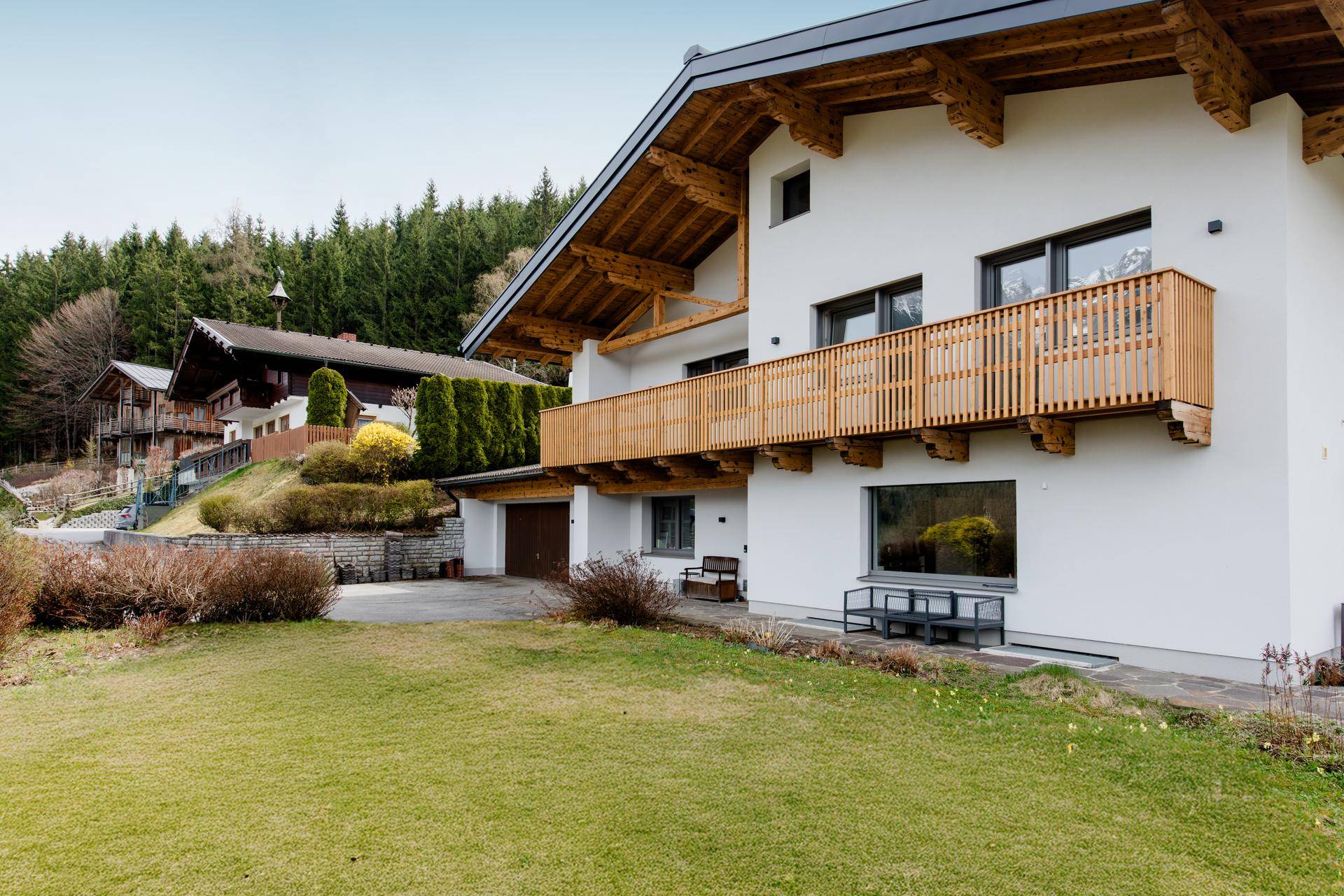 Modernes Haus mit Holzbalkon, gepflegtem Rasen und Blick auf die umliegende Natur.