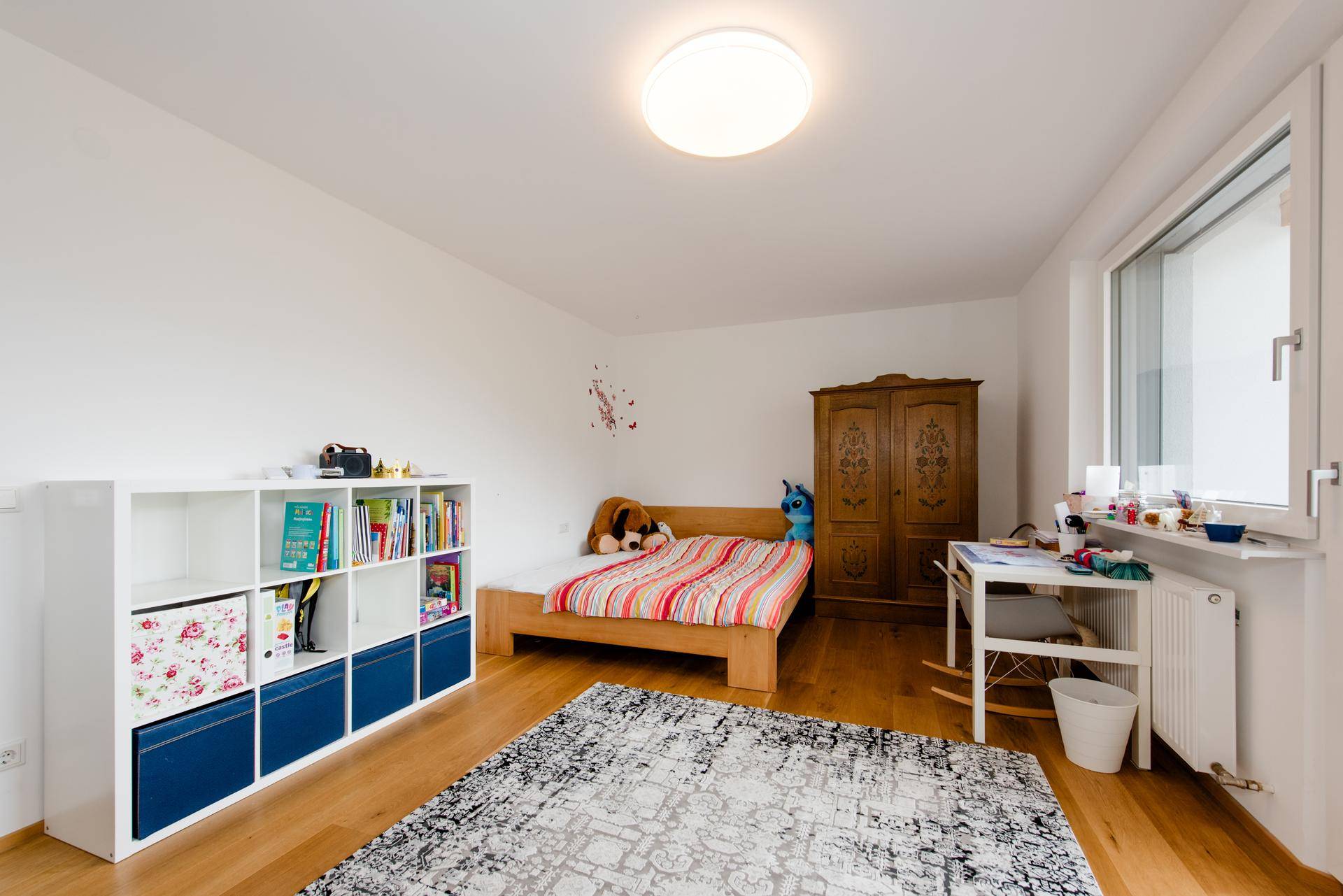Kinderzimmer mit Holzboden, Einzelbett, Schreibtisch und Bücherregal, hell und freundlich gestaltet.