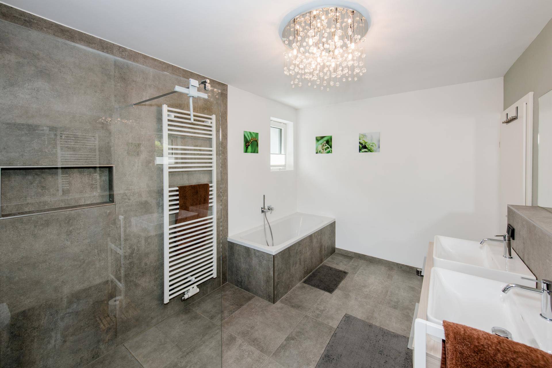 Modernes Badezimmer mit großer Dusche, Badewanne, Doppelwaschbecken und stilvoller Deckenleuchte.