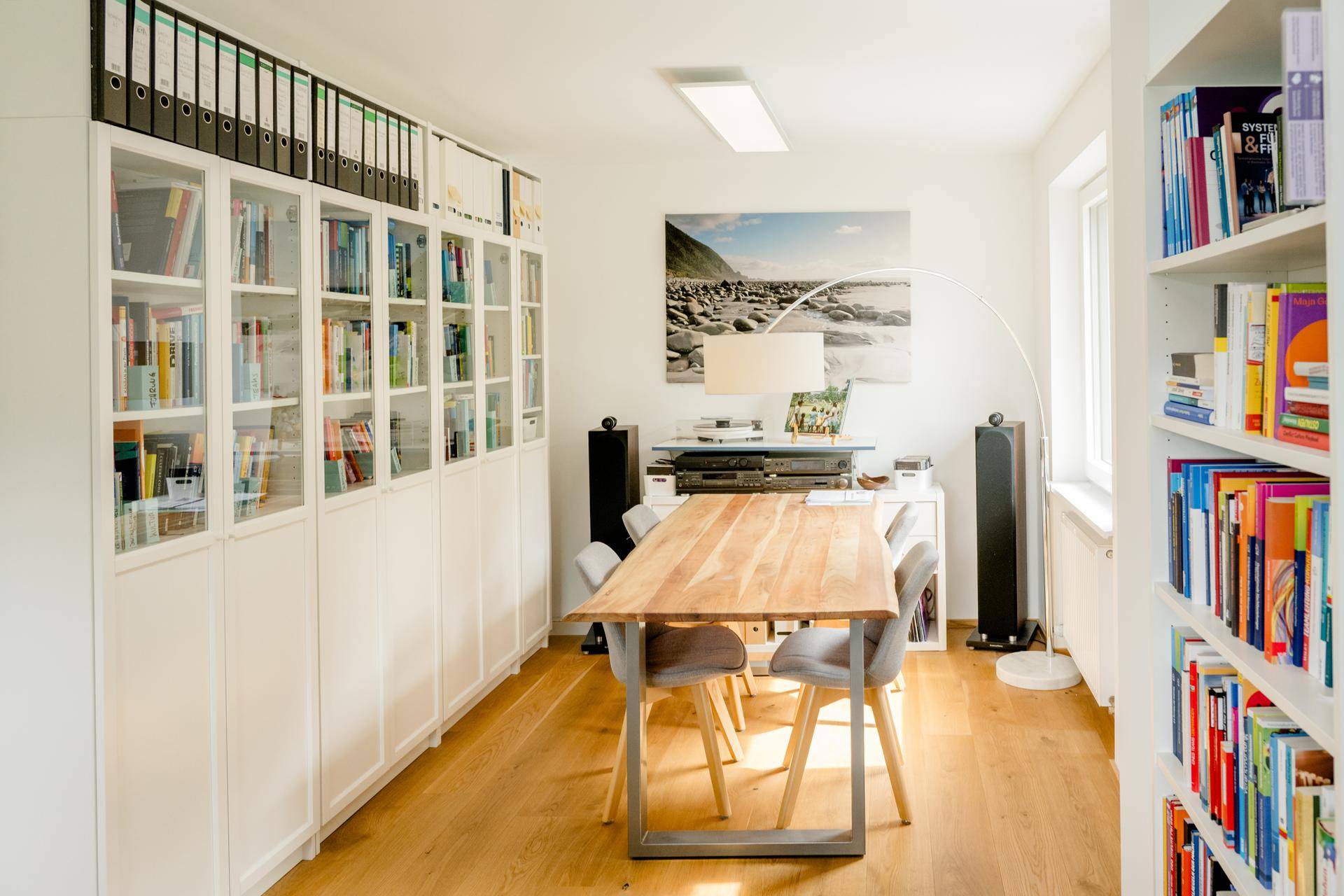 Arbeitszimmer mit umfangreichen Bücherregalen, Holztisch und moderner Beleuchtung, viel Stauraum.