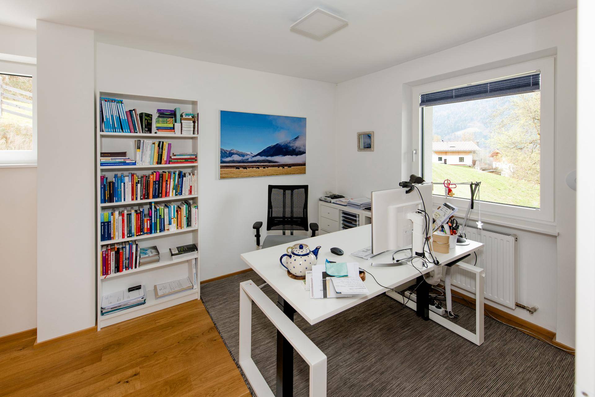 Helles Arbeitszimmer mit großem Schreibtisch, Bücherregal und Blick auf die umliegende Natur.