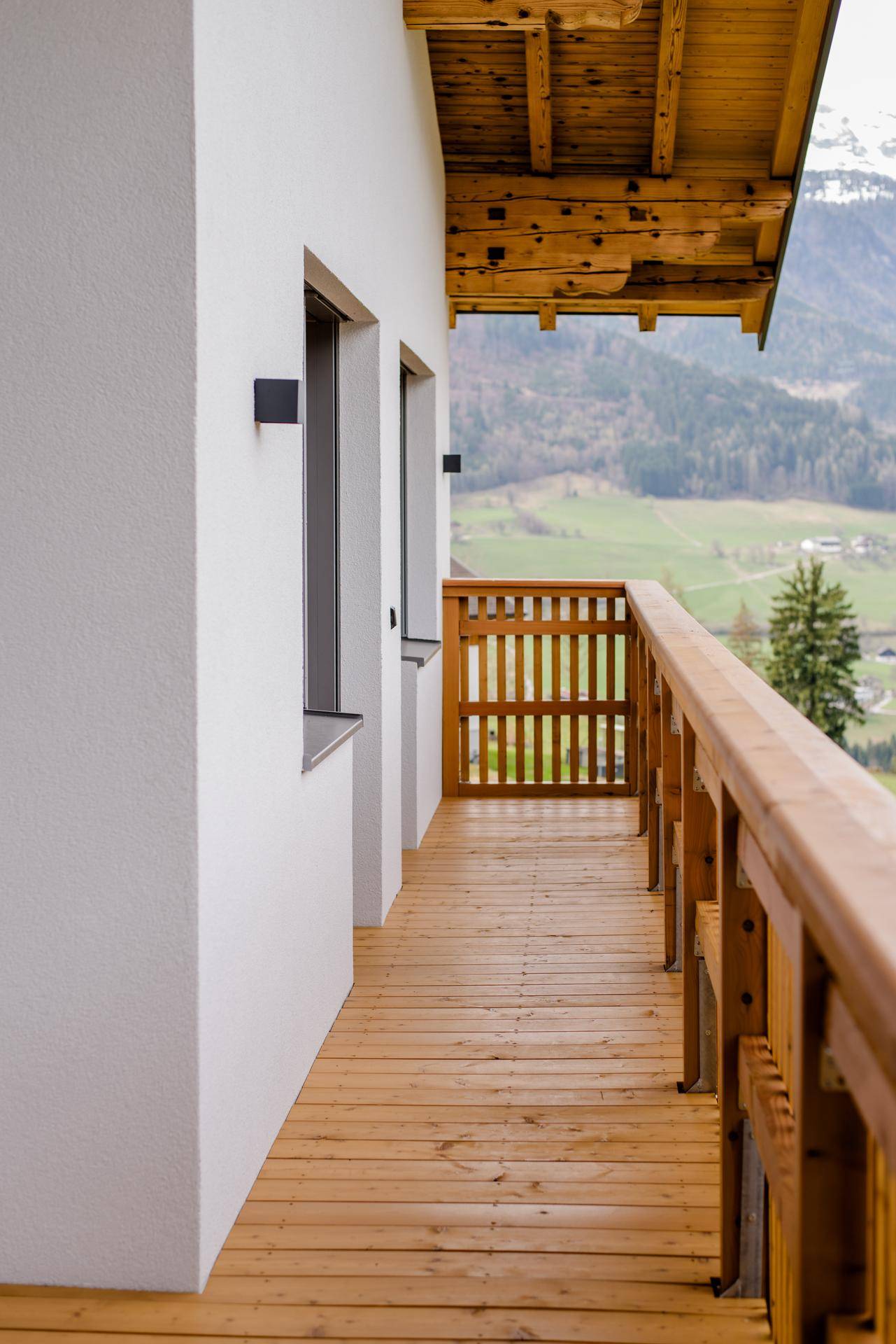 Langer Holzbalkon mit Geländer und Blick auf die umliegende Berglandschaft und Natur.