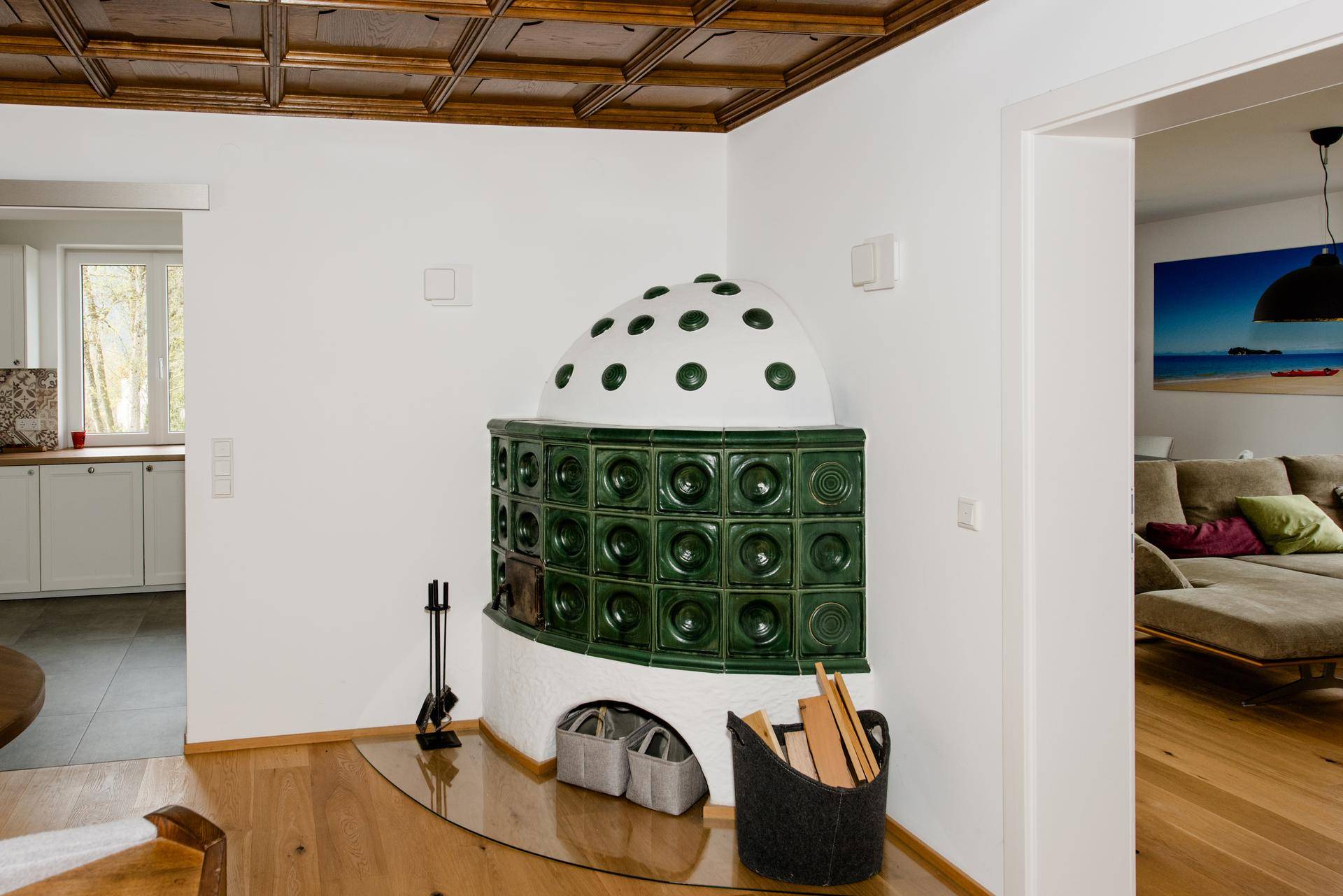 Traditioneller Kachelofen in einem Wohnbereich mit Holzboden und Kassettendecke, verbindet Ess- und Wohnzimmer.