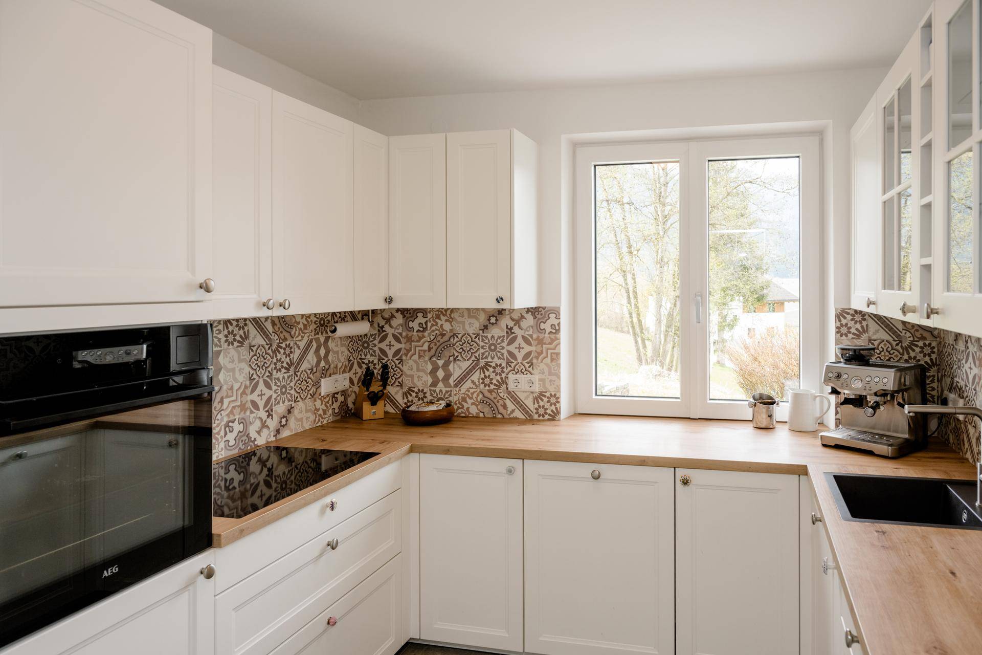 Helle Einbauküche mit weißen Schränken, Holz-Arbeitsplatte und Fenster mit Blick ins Grüne.