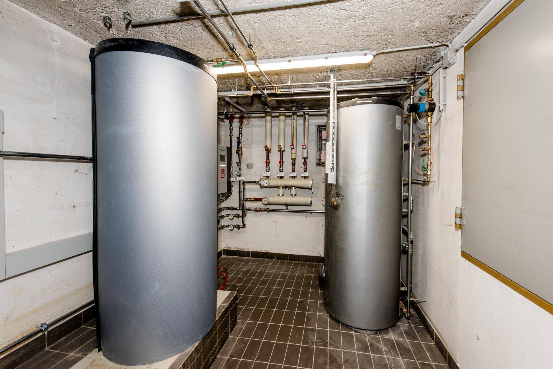 Heizungsraum mit zwei großen Warmwasserspeichern und sichtbaren Rohrleitungen.