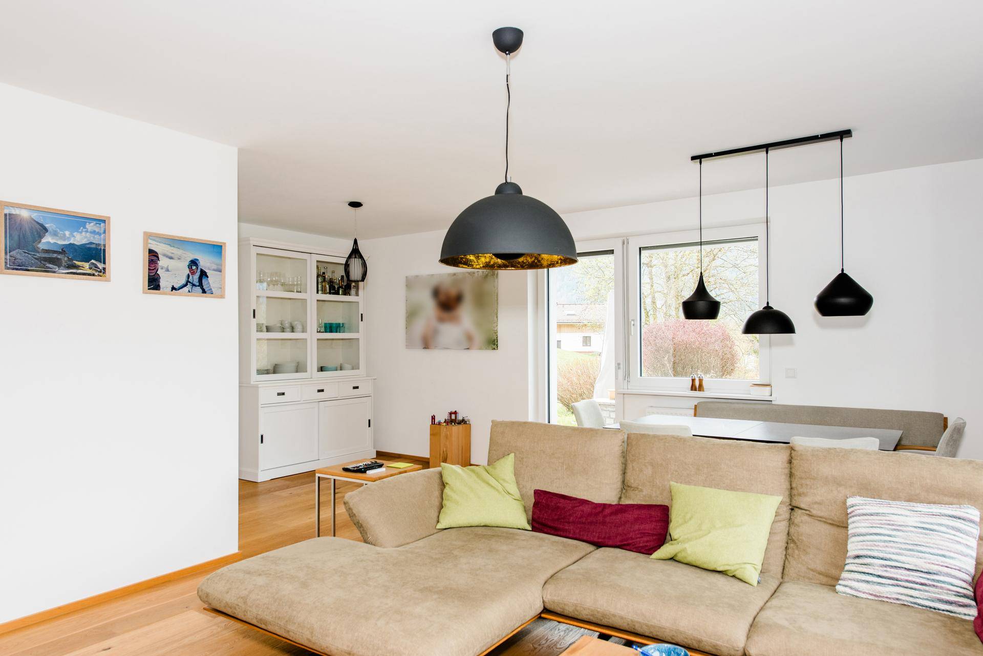 Geräumiger Wohnbereich mit beigem Ecksofa, modernen Pendelleuchten und Blick auf den Essbereich.