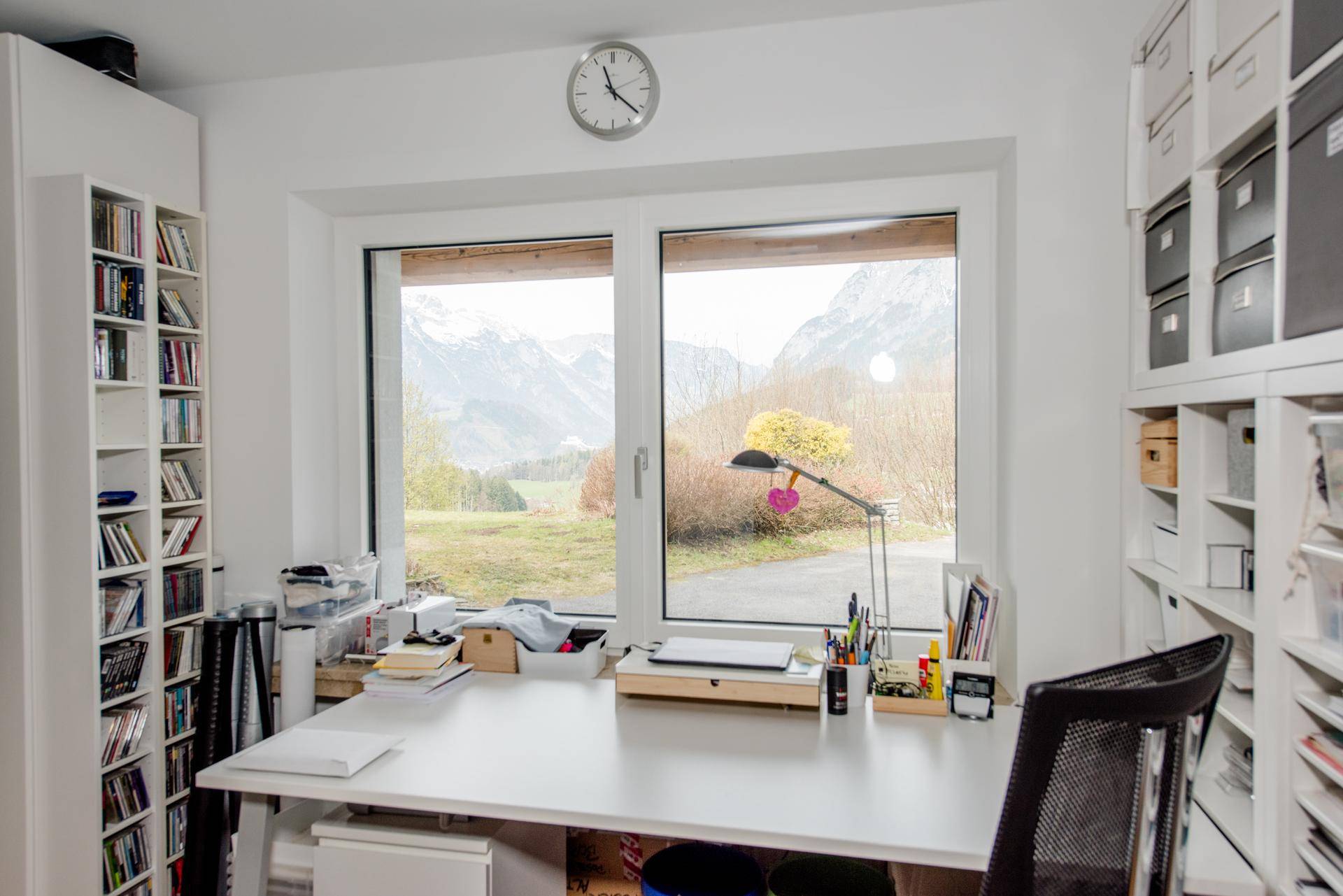 Heller Hobbyraum mit großem Fenster, Schreibtisch und Regalen, bietet viel Stauraum und Arbeitsfläche.