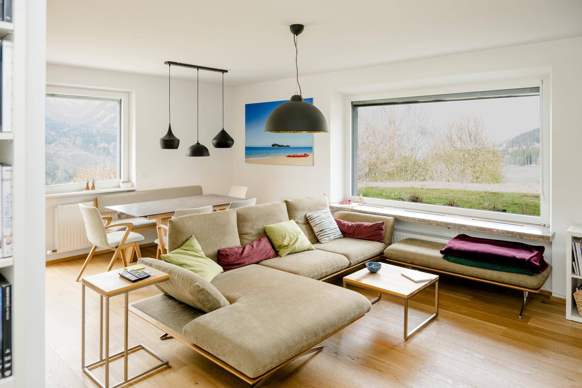 Helles Wohn-Esszimmer mit beigem Ecksofa, Holzboden und großem Fenster mit Landschaftsblick.
