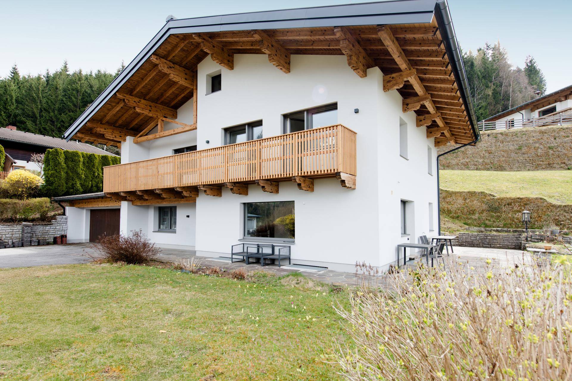 Attraktives Haus mit Holzbalkon, gepflegtem Rasen und Sitzgelegenheiten im Freien.