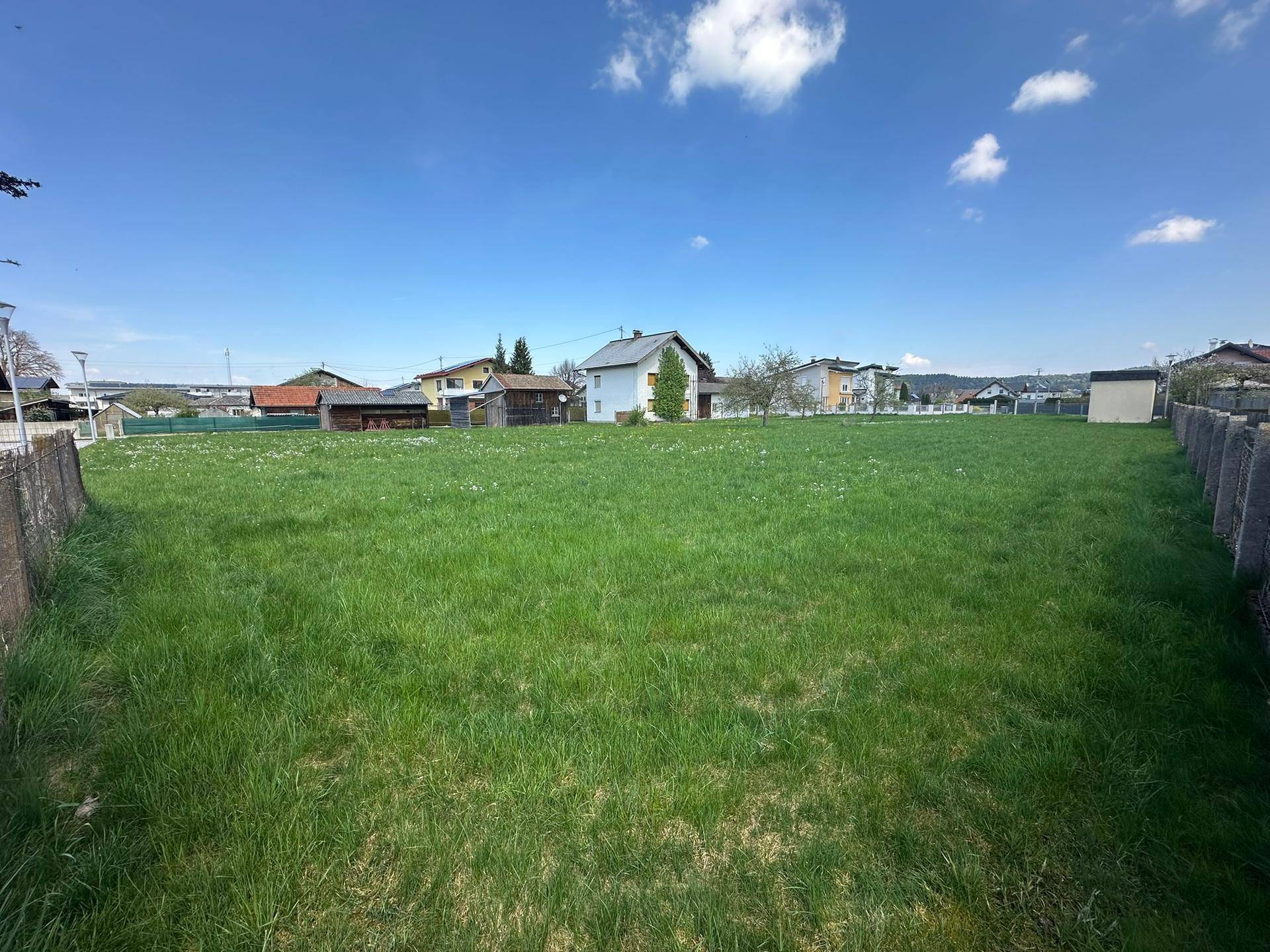 Weitläufiges grünes Grundstück mit Blick auf die umliegende Wohnbebauung und einen Schuppen.