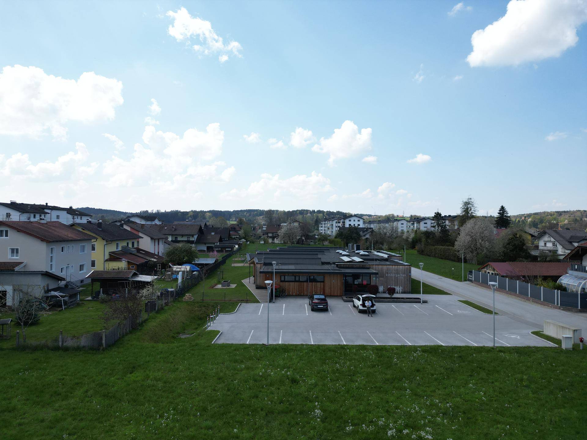 Luftaufnahme einer Wohngegend mit einem modernen Gebäude und Parkplätzen im Vordergrund.