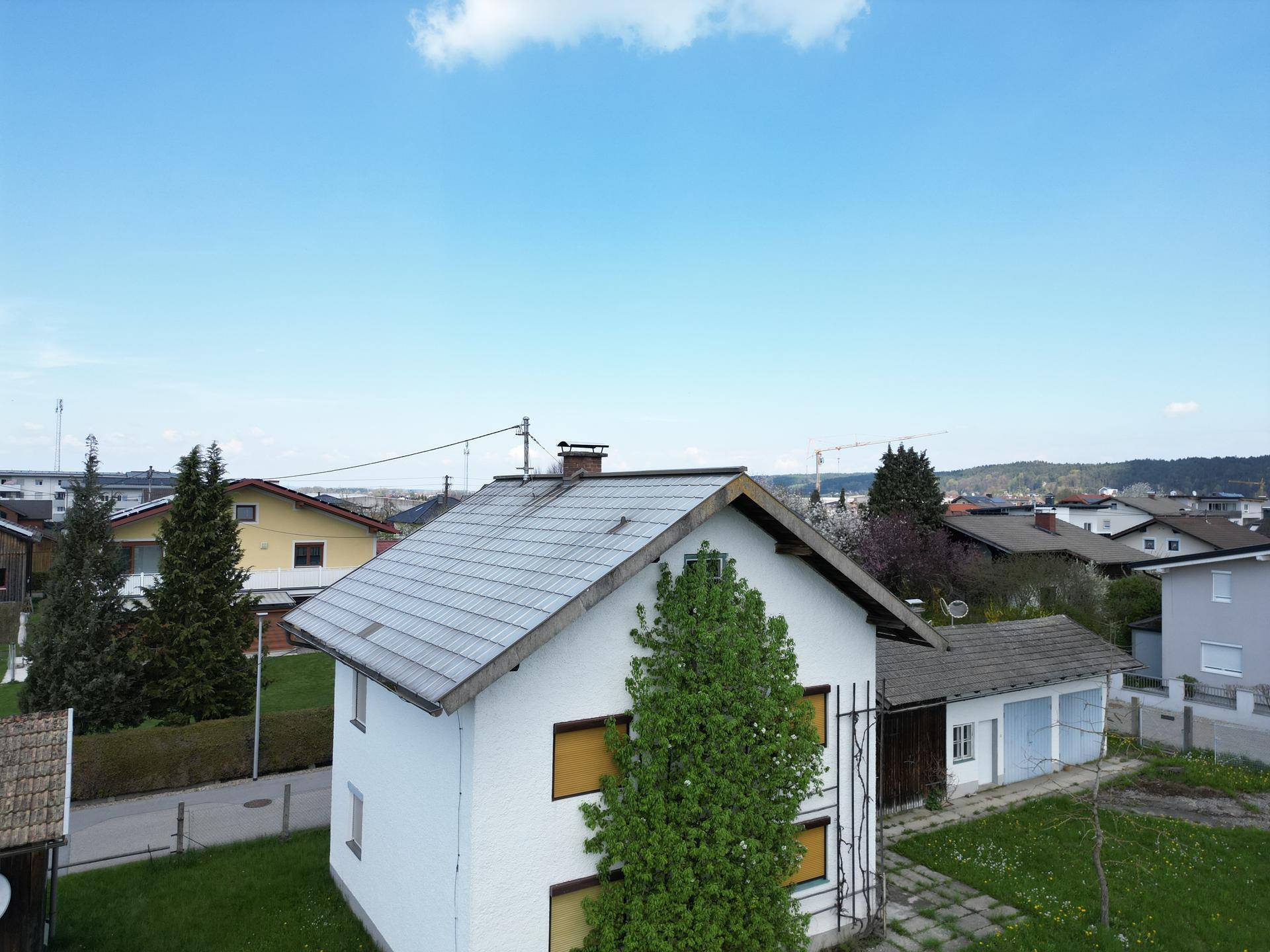 Luftaufnahme eines Wohnhauses mit Satteldach und umliegender Nachbarschaft unter blauem Himmel.