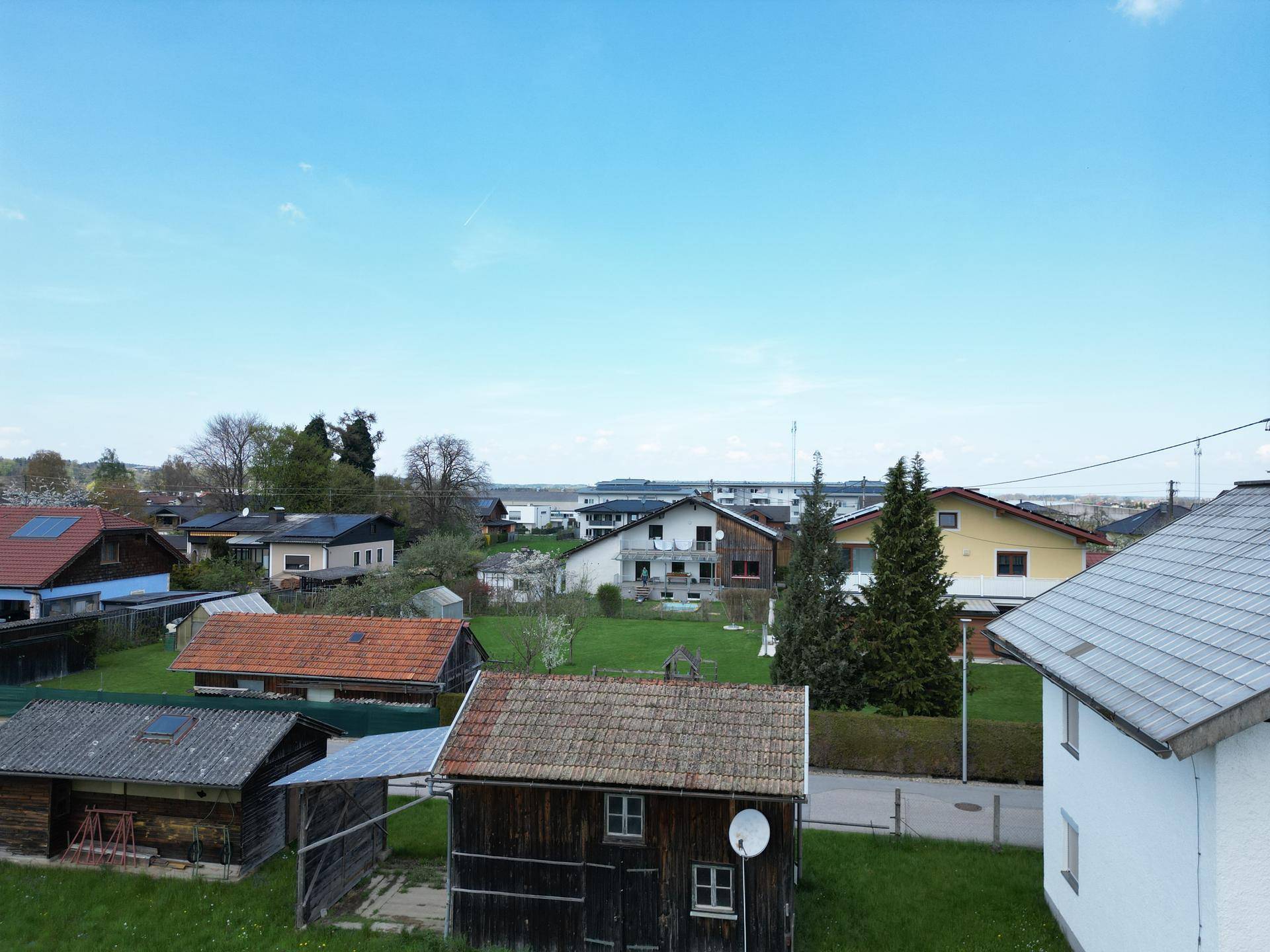 Luftaufnahme einer Wohnsiedlung mit älteren Schuppen und Häusern unter blauem Himmel.