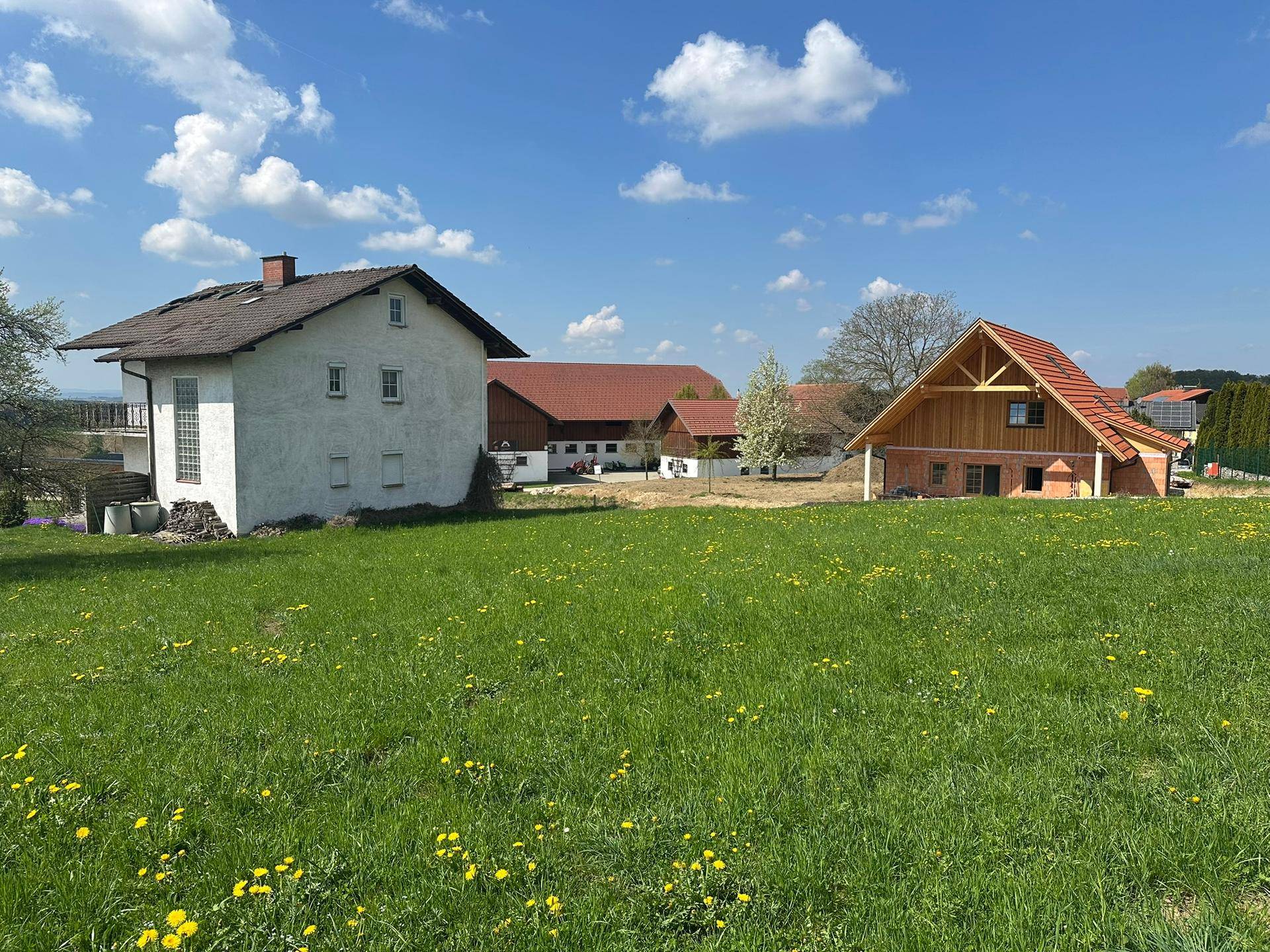Ländliches Anwesen mit traditionellen Gebäuden, roten Dächern und einem Neubau im Vordergrund.