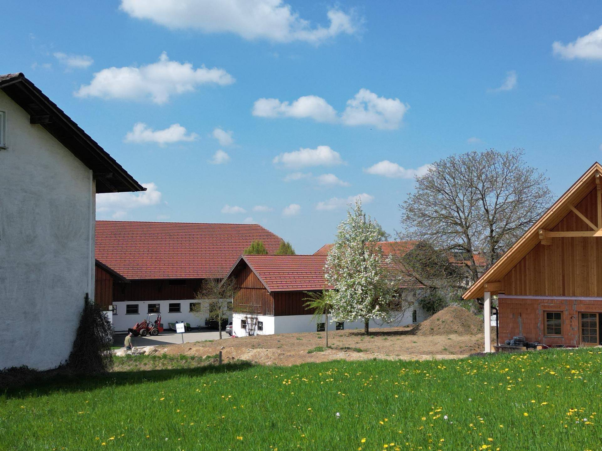 Ländliches Anwesen mit mehreren Gebäuden, roten Dächern und blühenden Bäumen im Frühling.