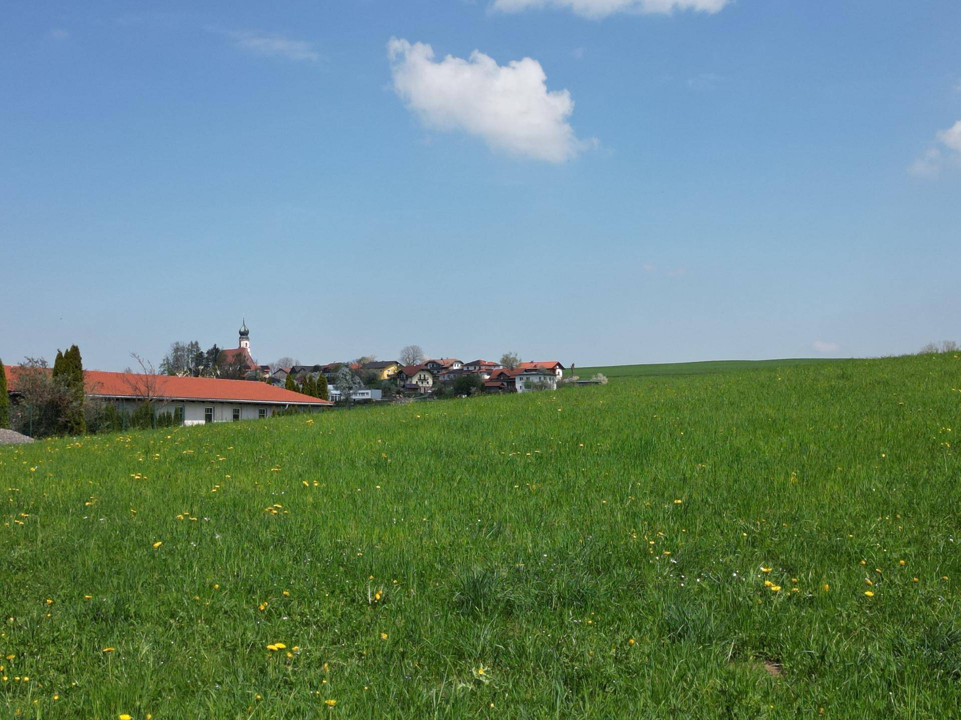 Grüne Wiesen im Vordergrund mit einem malerischen Dorf und Kirchturm in der Ferne.