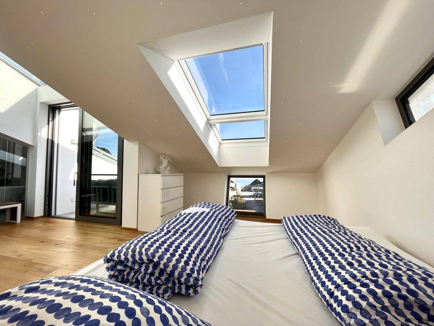 Helles Schlafzimmer mit Holzboden, Dachfenstern und Zugang zu einem Balkon.