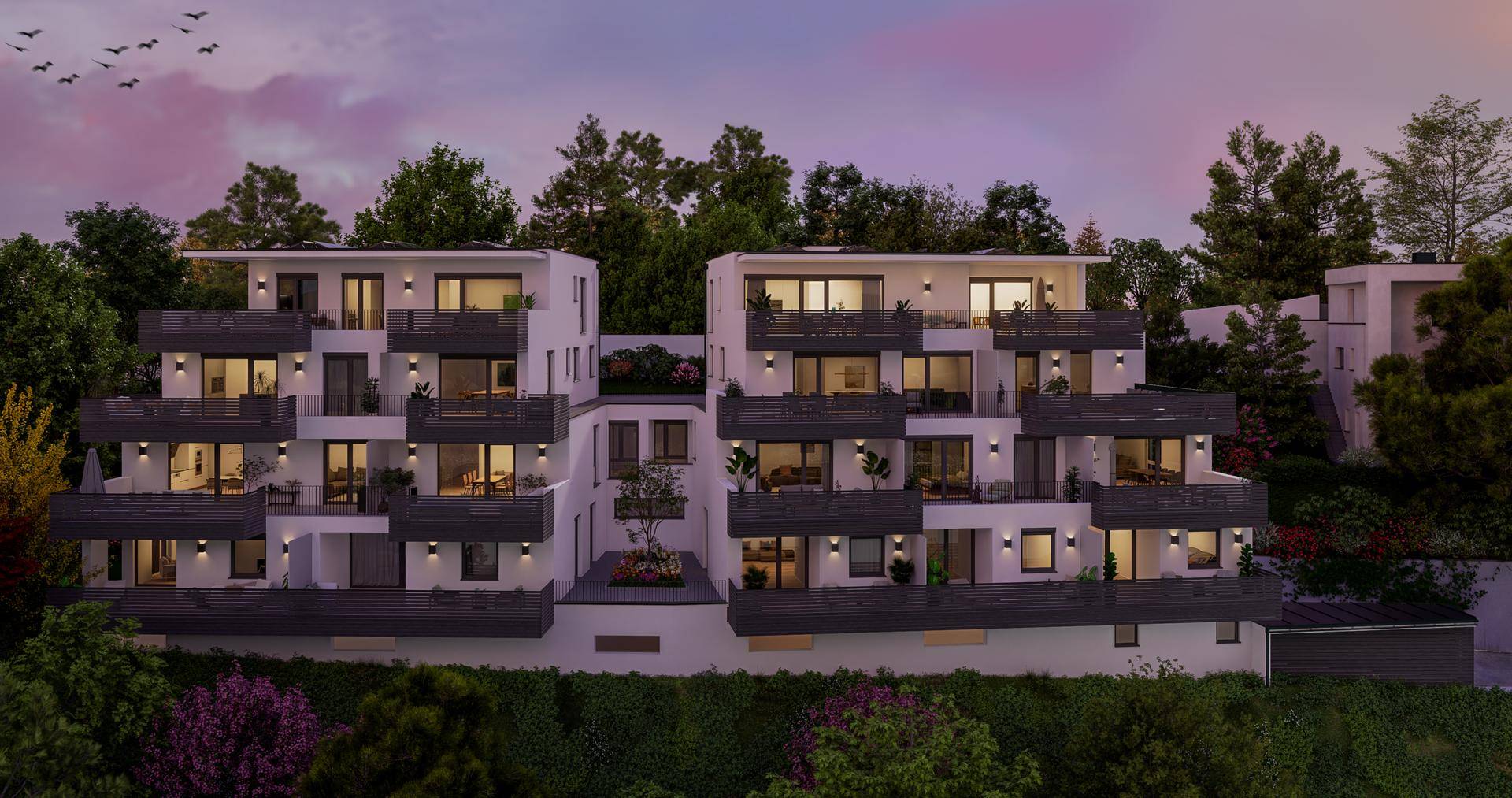 Moderne Wohnanlage bei Sonnenuntergang, umgeben von Bäumen, mit beleuchteten Balkonen und Terrassen.