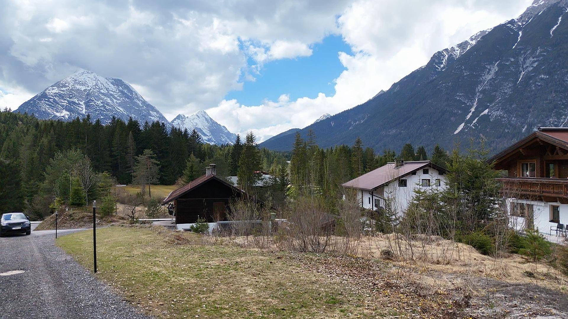 Weitläufige alpine Landschaft mit Häusern, Straße und beeindruckenden schneebedeckten Bergen im Hintergrund.