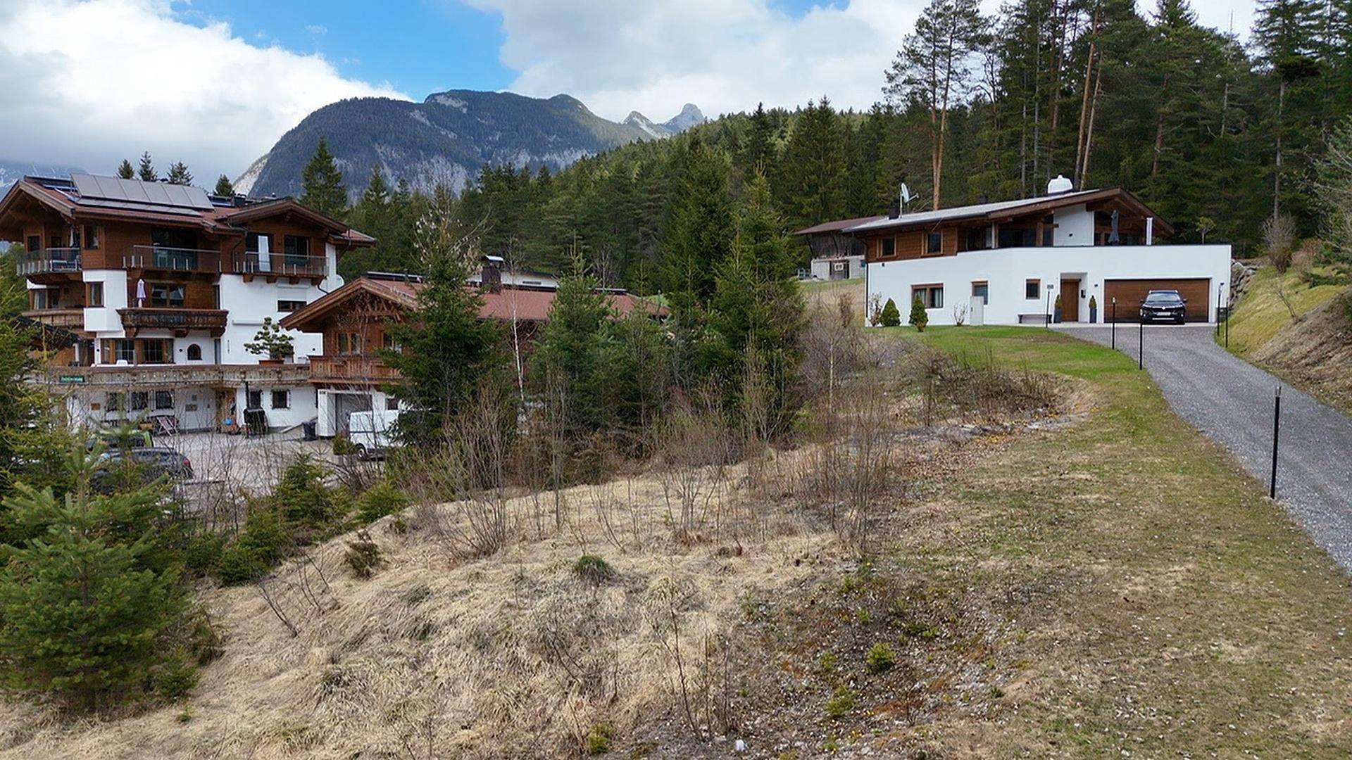 Panoramablick auf mehrere Häuser in alpiner Umgebung mit bewaldeten Hängen und Bergen.