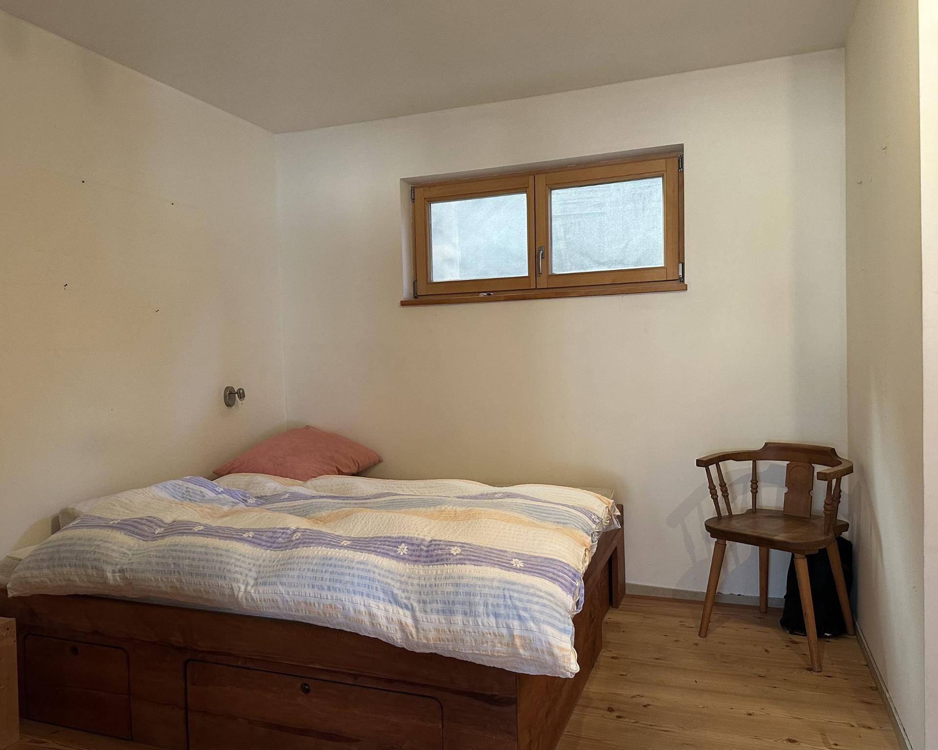 Gemütliches Schlafzimmer mit Holzbett, kleinem Fenster und einfacher, funktionaler Einrichtung.