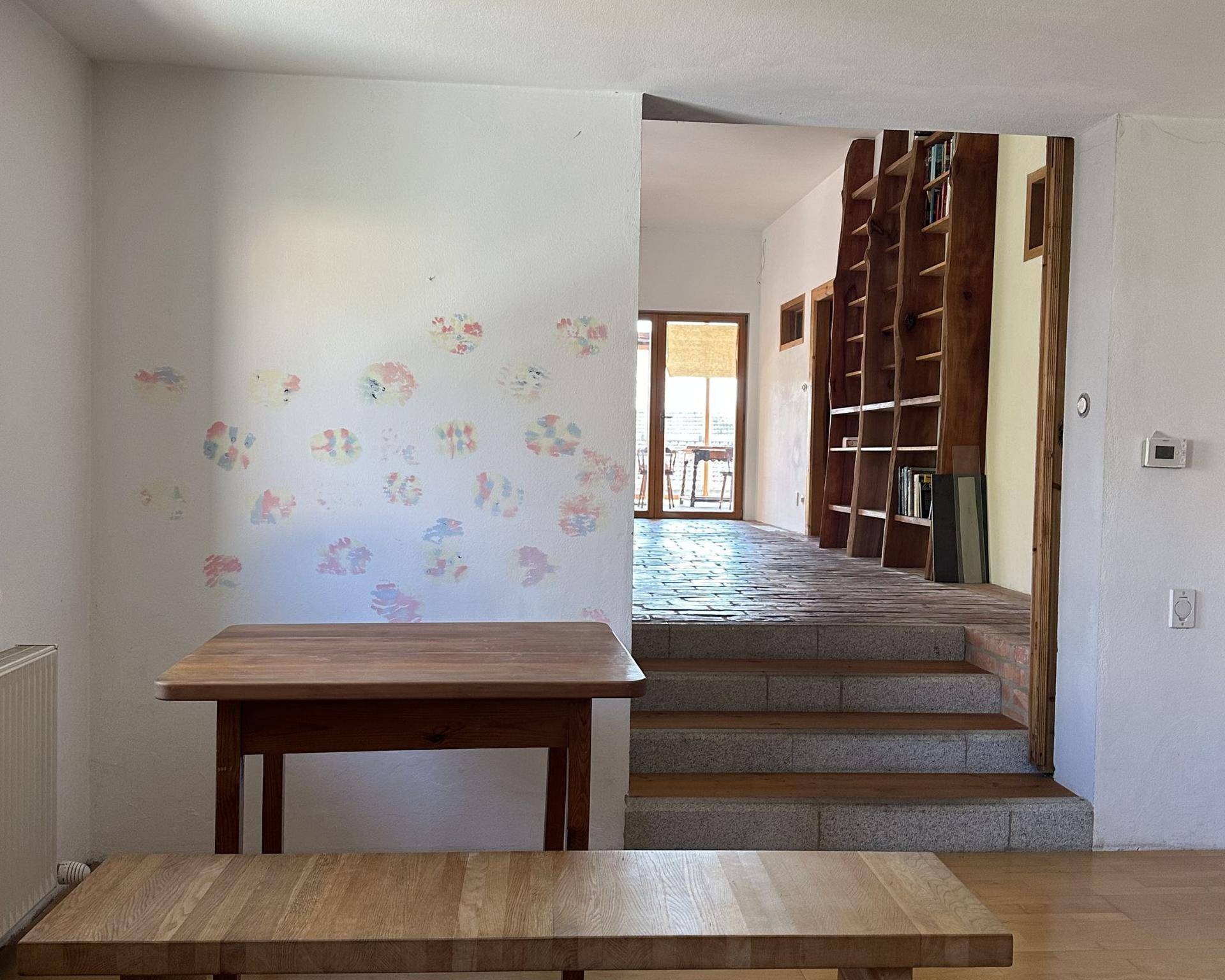 Heller Innenraum mit Holztisch, Treppe und einem großen, eingebauten Bücherregal aus Holz.