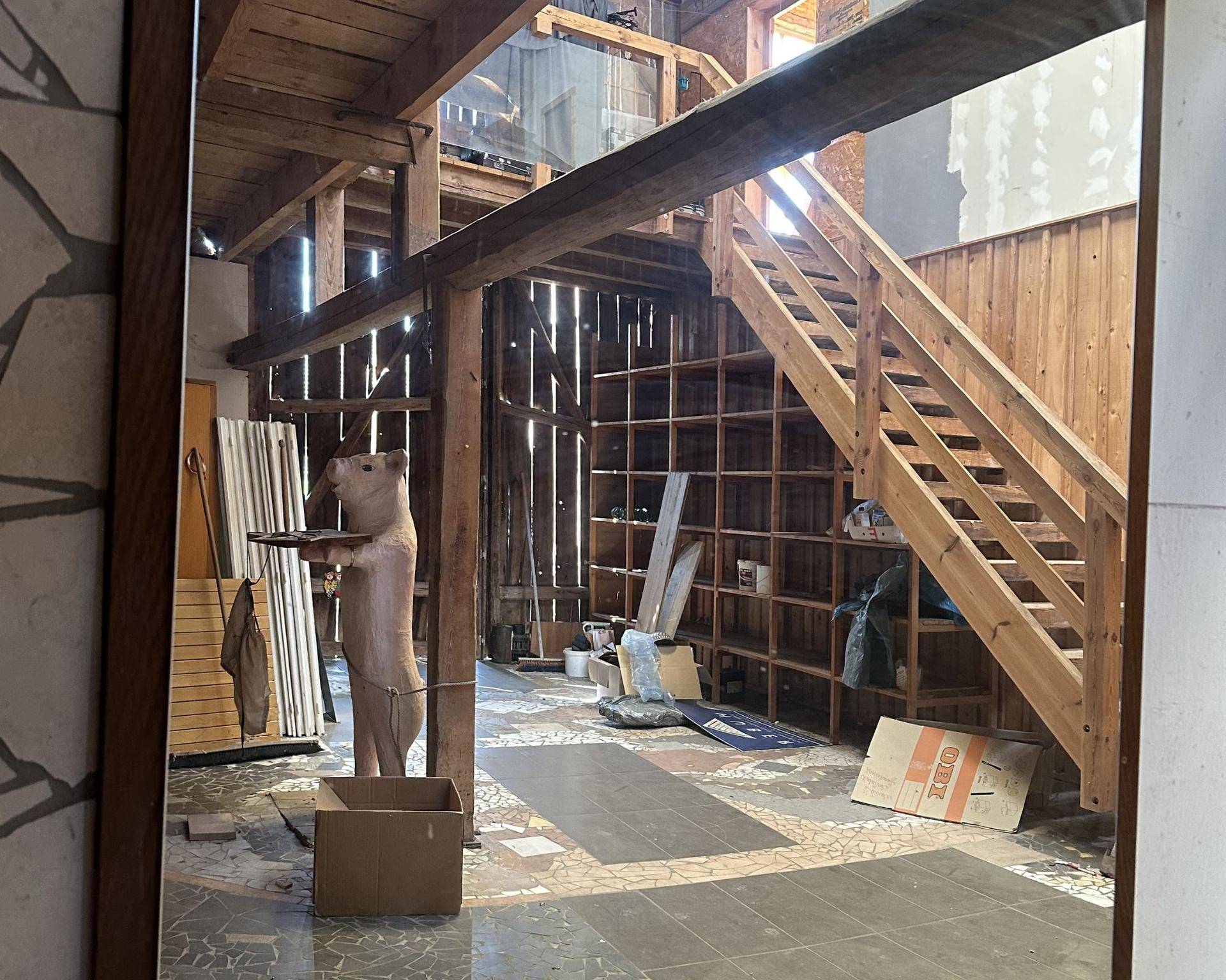 Unfertiger Innenraum mit Holzbalken, Treppe und Regalen, der auf einen Ausbau wartet.
