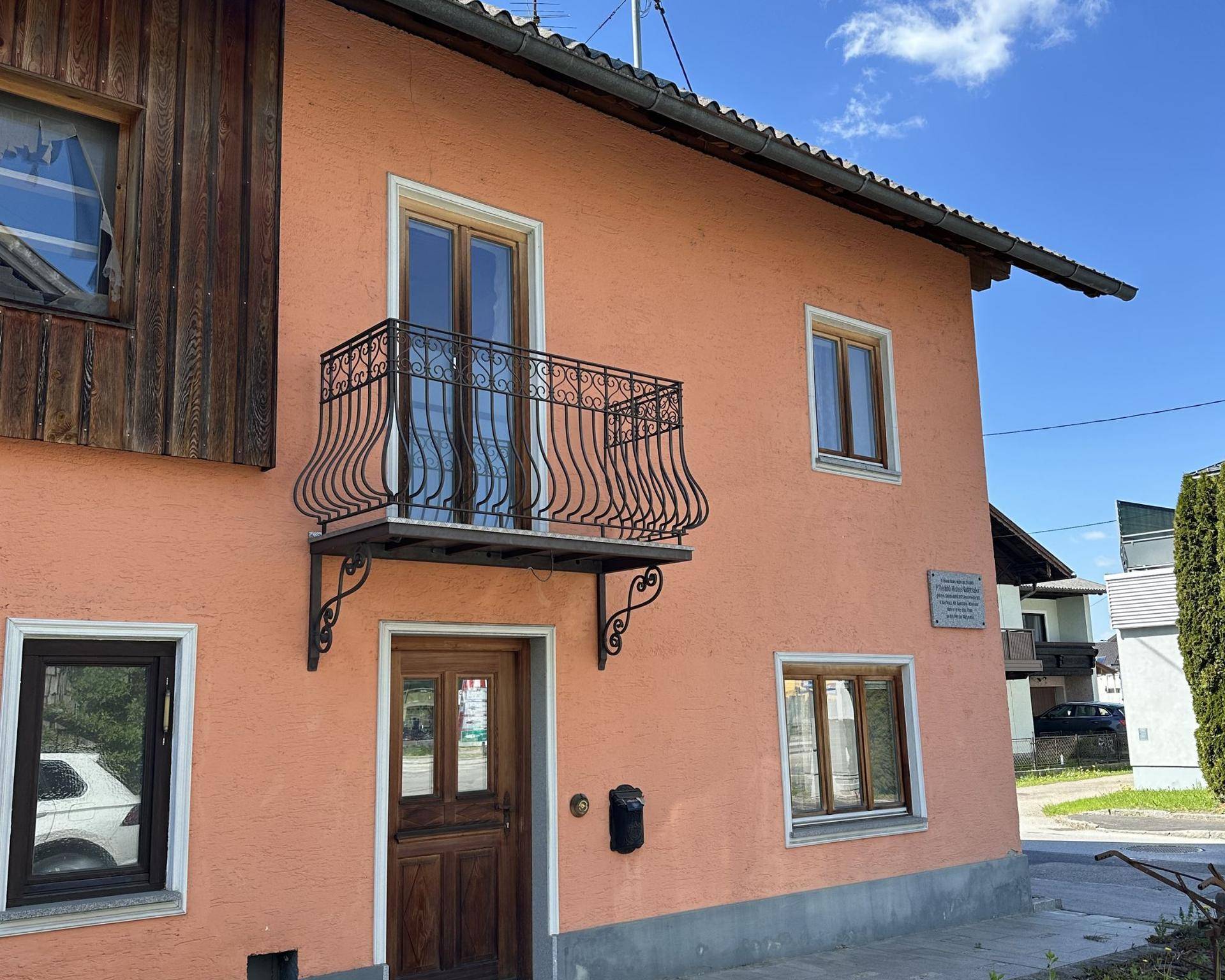 Vorderansicht eines Hauses mit rosafarbener Fassade, Holztür und einem französischen Balkon.