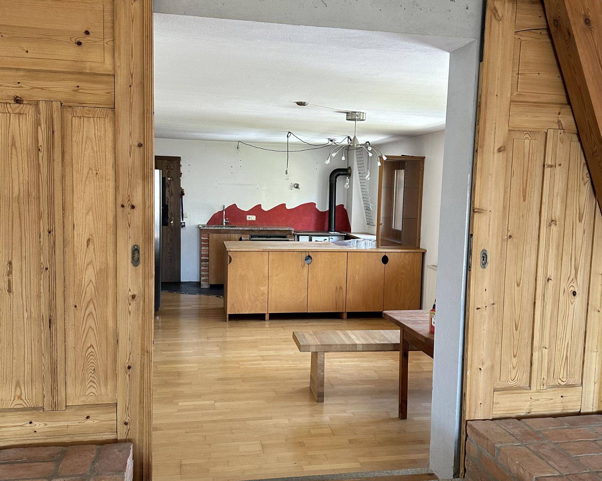 Blick durch eine Holztür in eine geräumige Küche mit hellem Holzfußboden und rustikalen Elementen.