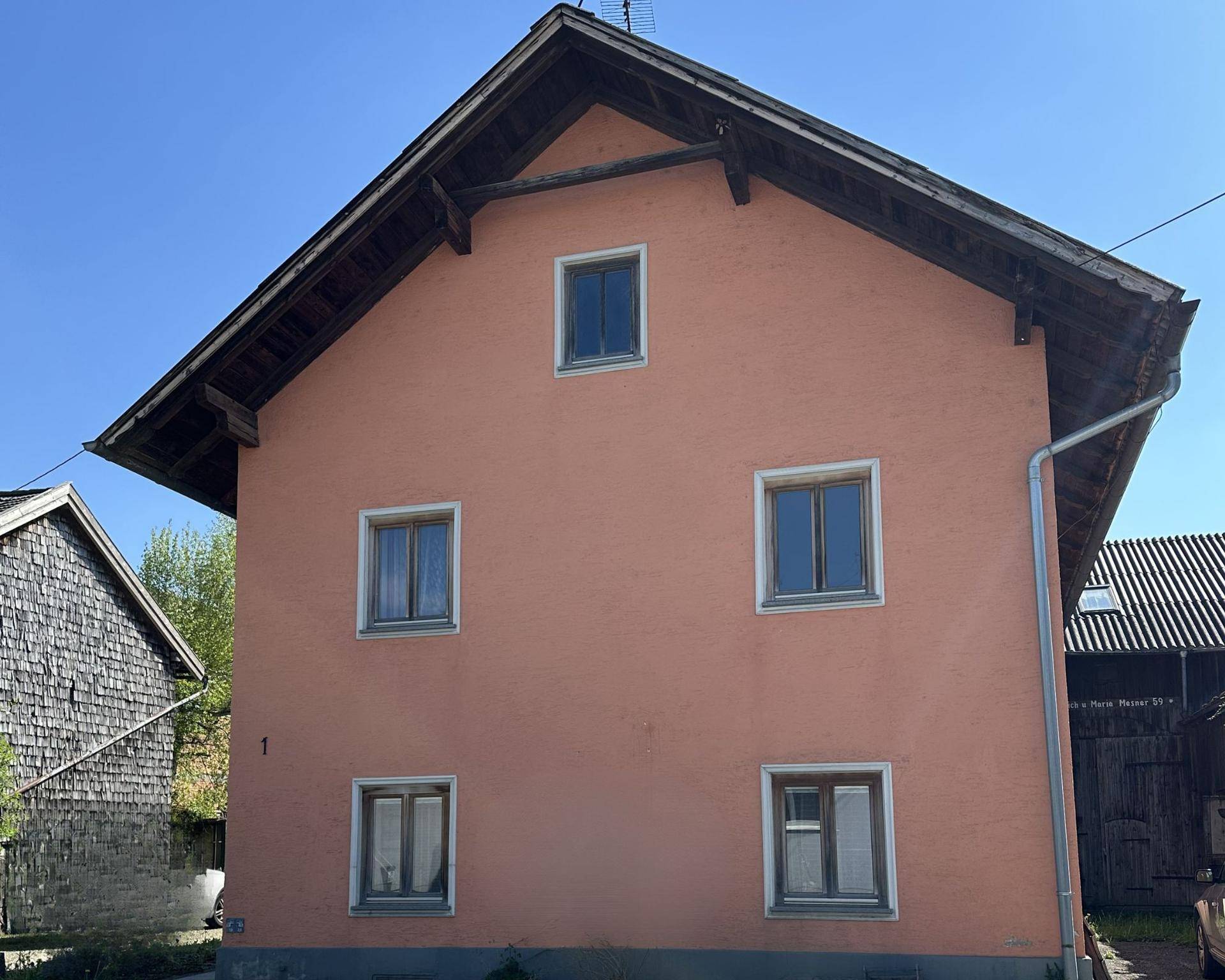 Seitenansicht eines Wohnhauses mit rosafarbener Fassade und Satteldach unter blauem Himmel.