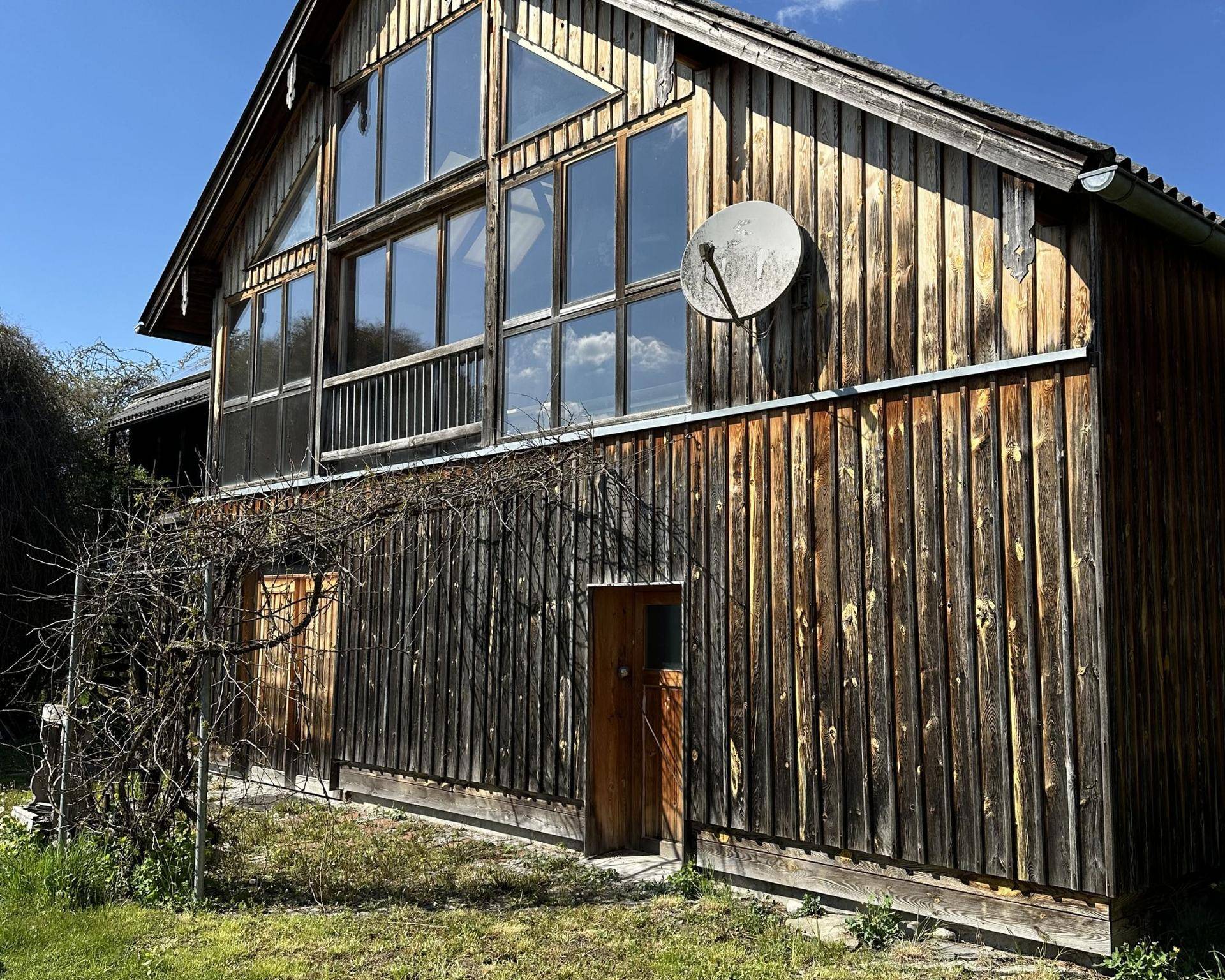 Holzfassade des Gebäudes mit großen Fensterfronten und einer Satellitenschüssel unter blauem Himmel.