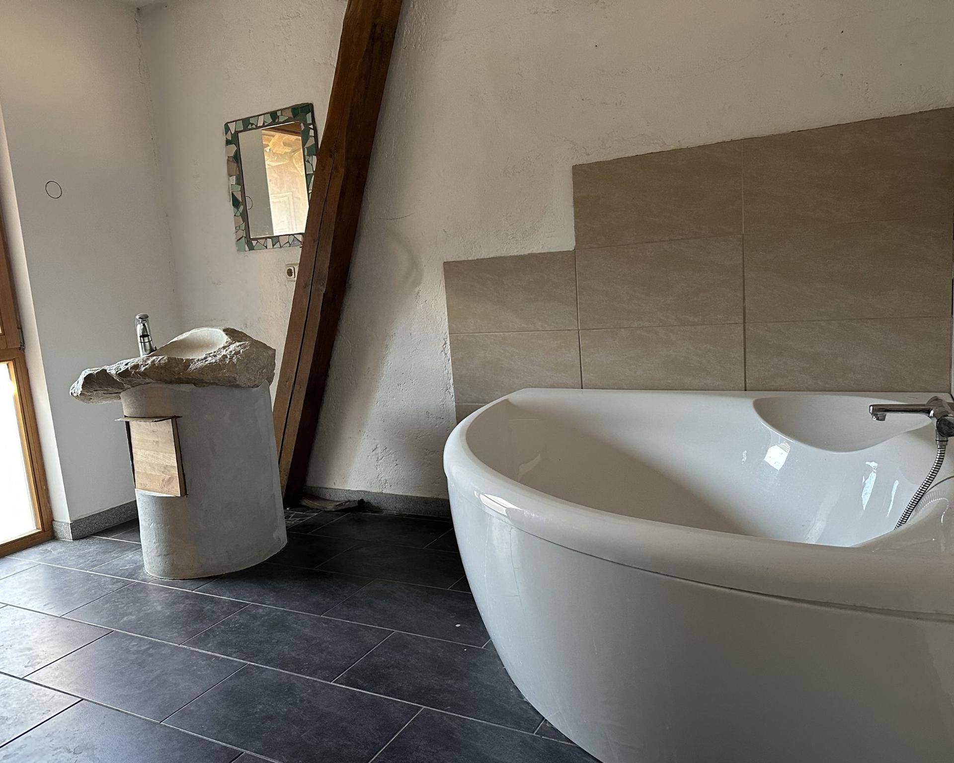 Individuelles Badezimmer mit freistehender Badewanne, einzigartigem Steinwaschbecken und Holzbalken.