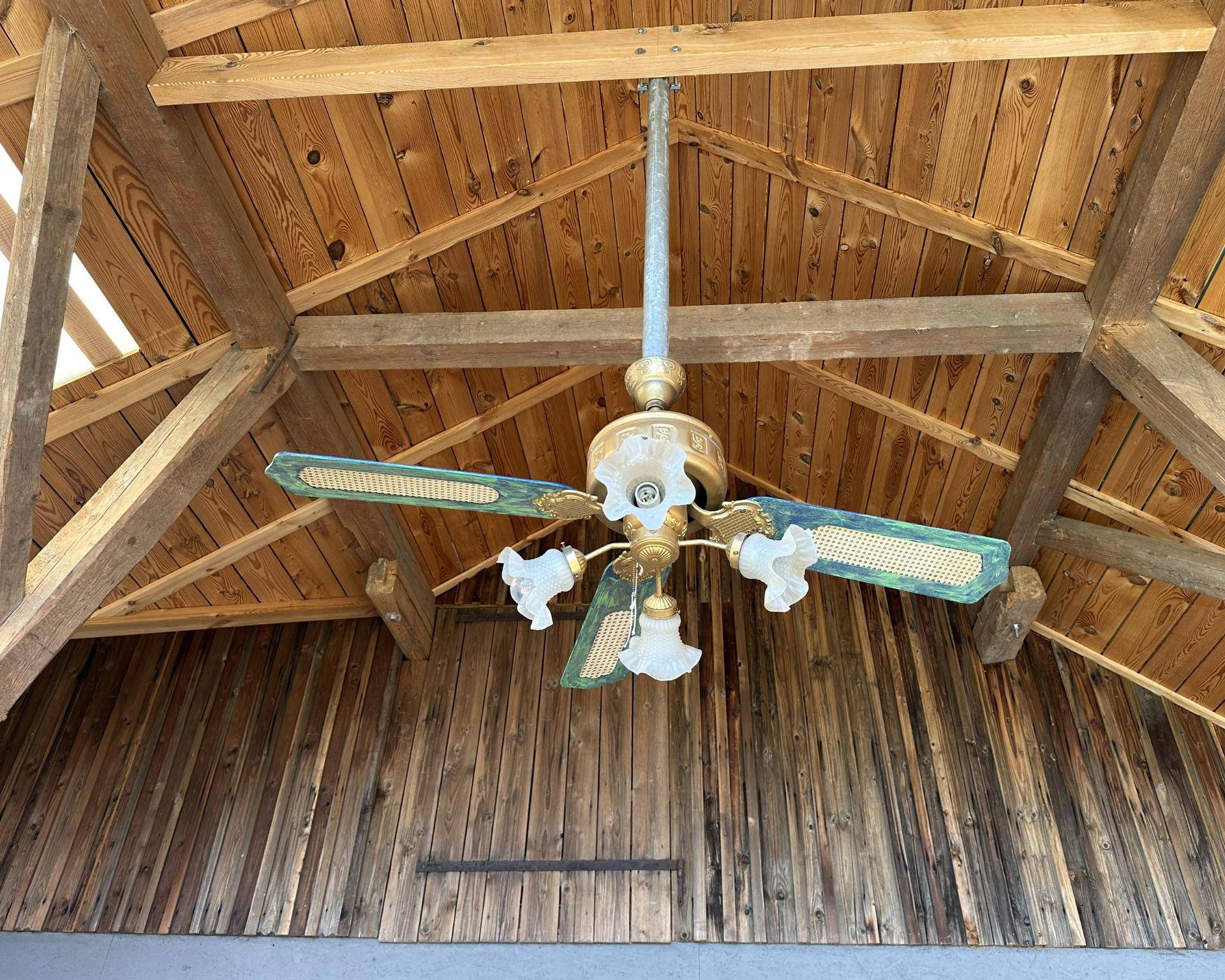 Deckenventilator mit Beleuchtung unter einer Holzdecke mit sichtbaren Balken und hoher Decke.
