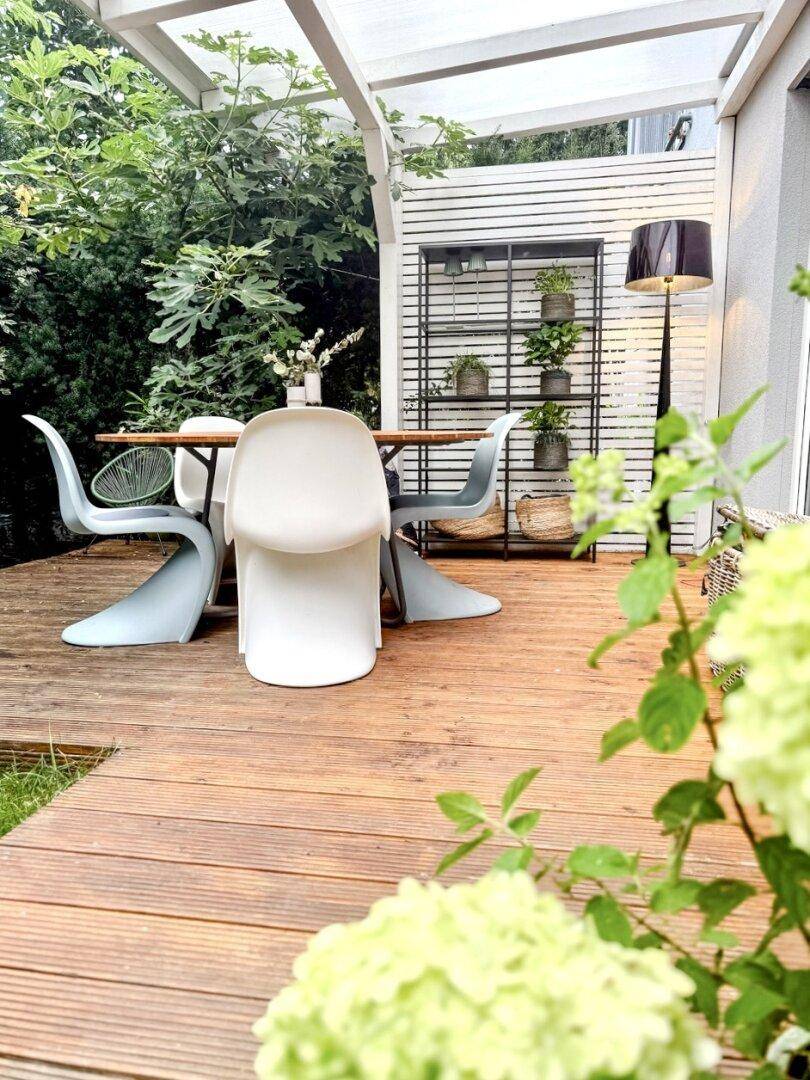 Detailansicht der Holzterrasse mit moderner Sitzgruppe und üppiger Bepflanzung im Hintergrund.
