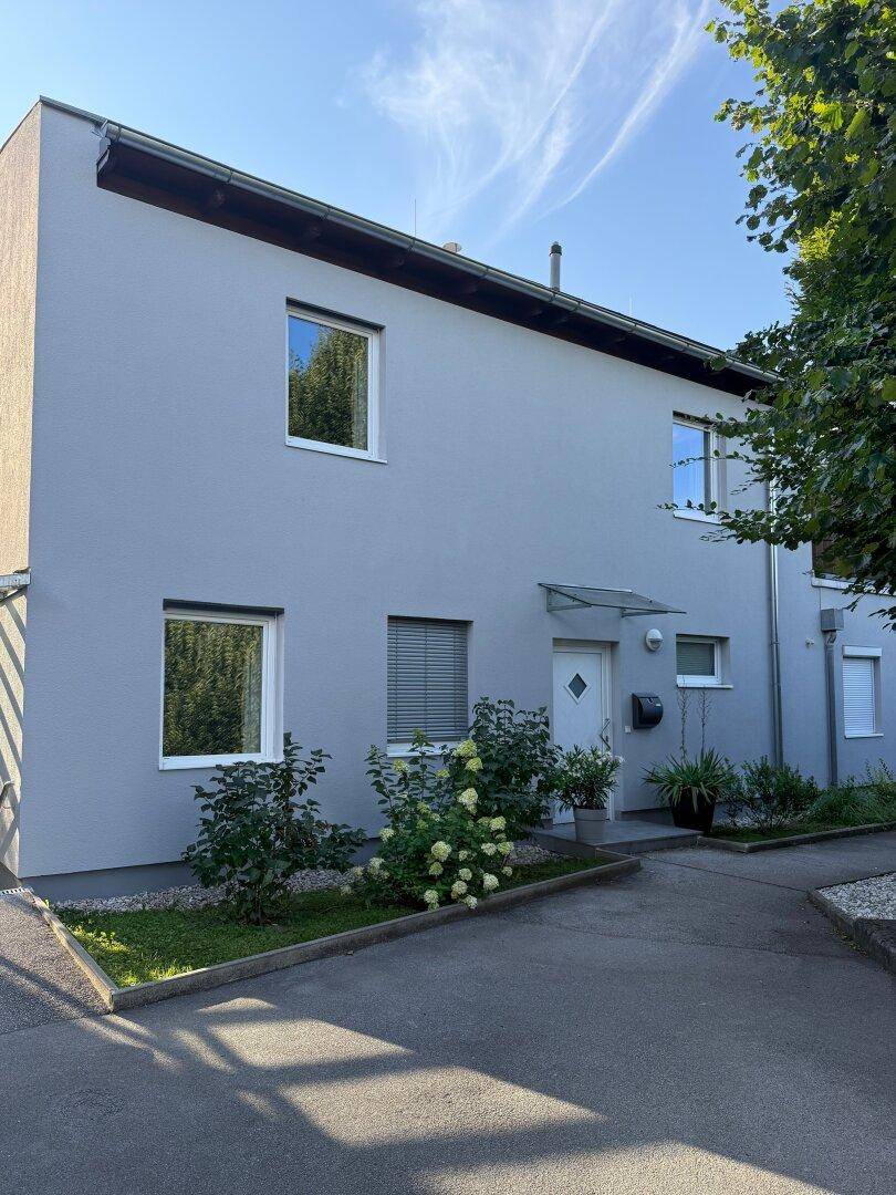 Moderne Hausfassade in Grau mit weißen Fenstern und gepflegtem Eingangsbereich.
