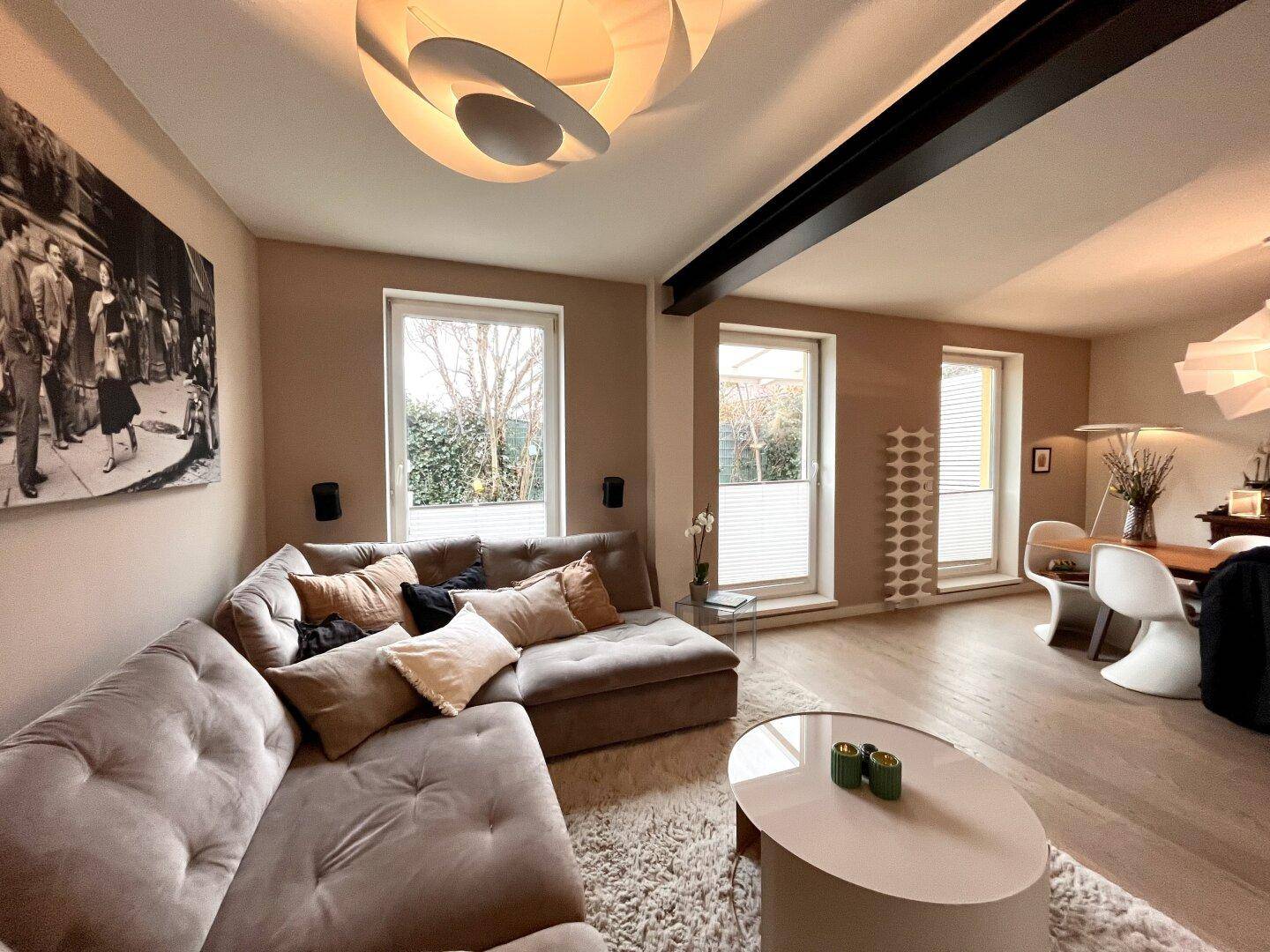 Helles Wohn- und Esszimmer mit beigem Sofa, Holzboden und modernen Leuchten.