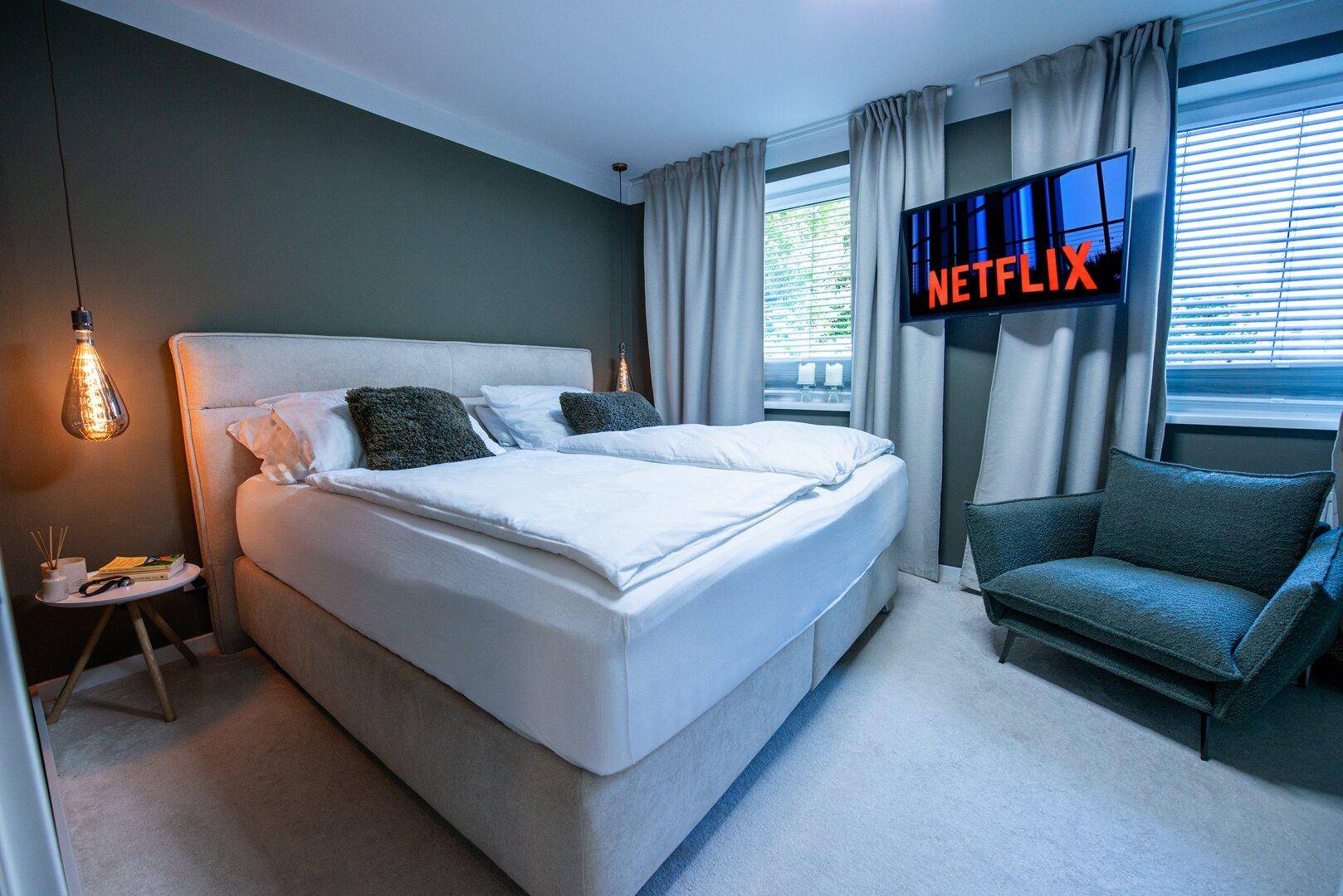 Gemütliches Schlafzimmer mit großem Bett, Wandfernseher und dunklen Wänden für eine entspannte Atmosphäre.