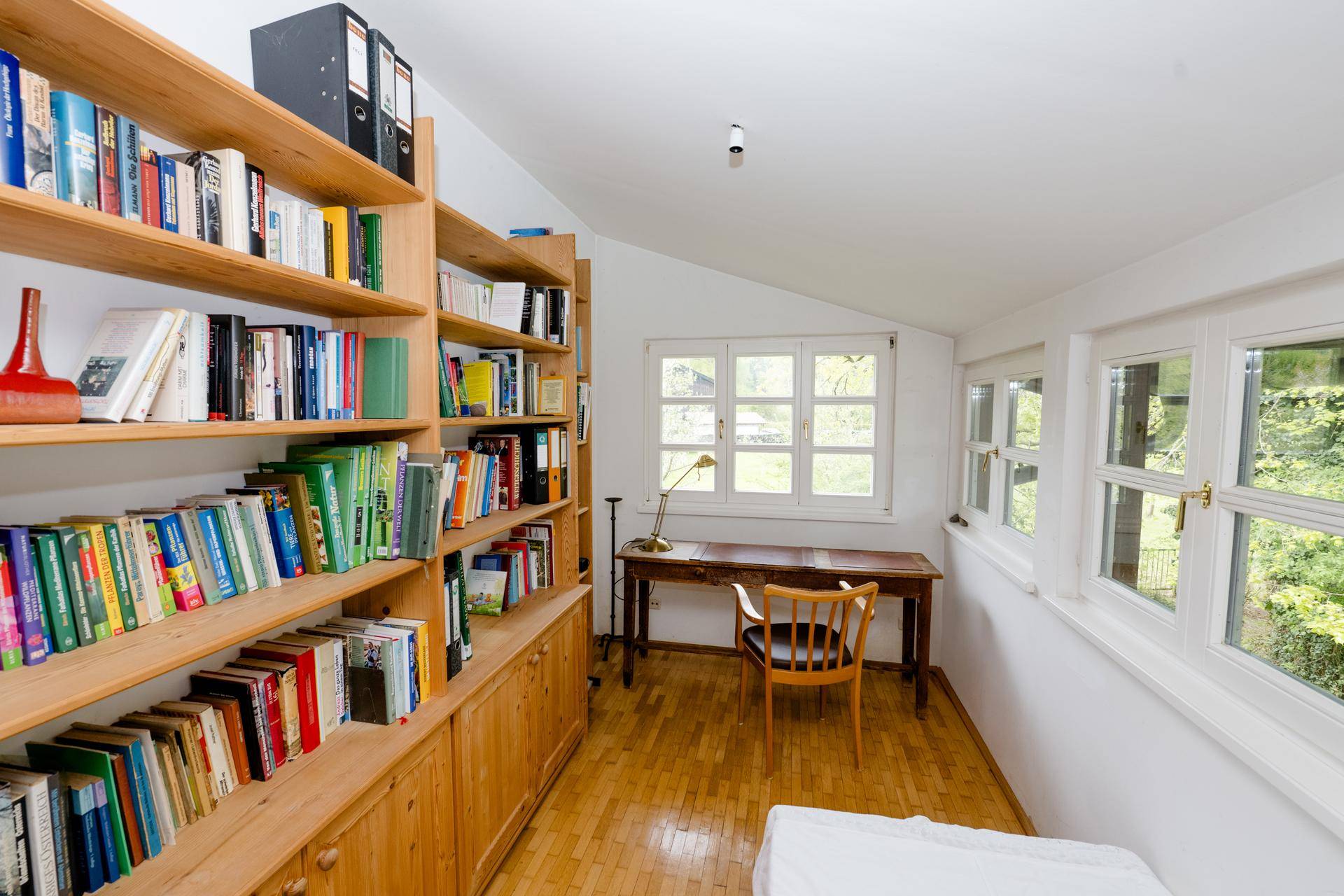 Helles Arbeitszimmer mit Holzboden, Bücherregalen und einem Schreibtisch am Fenster.