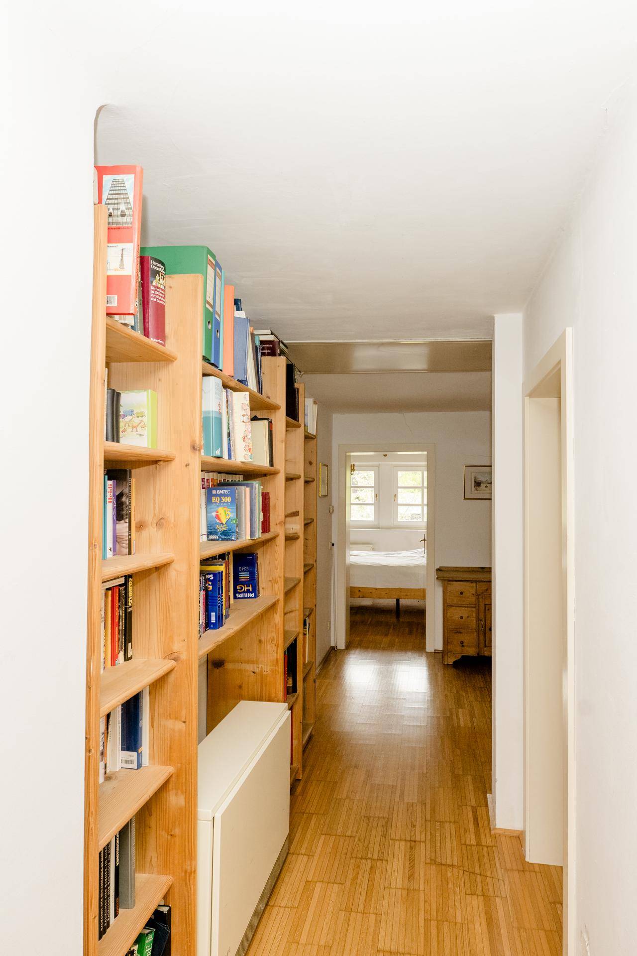 Heller Flur mit Holzboden und langen Bücherregalen, der zu weiteren Räumen führt.