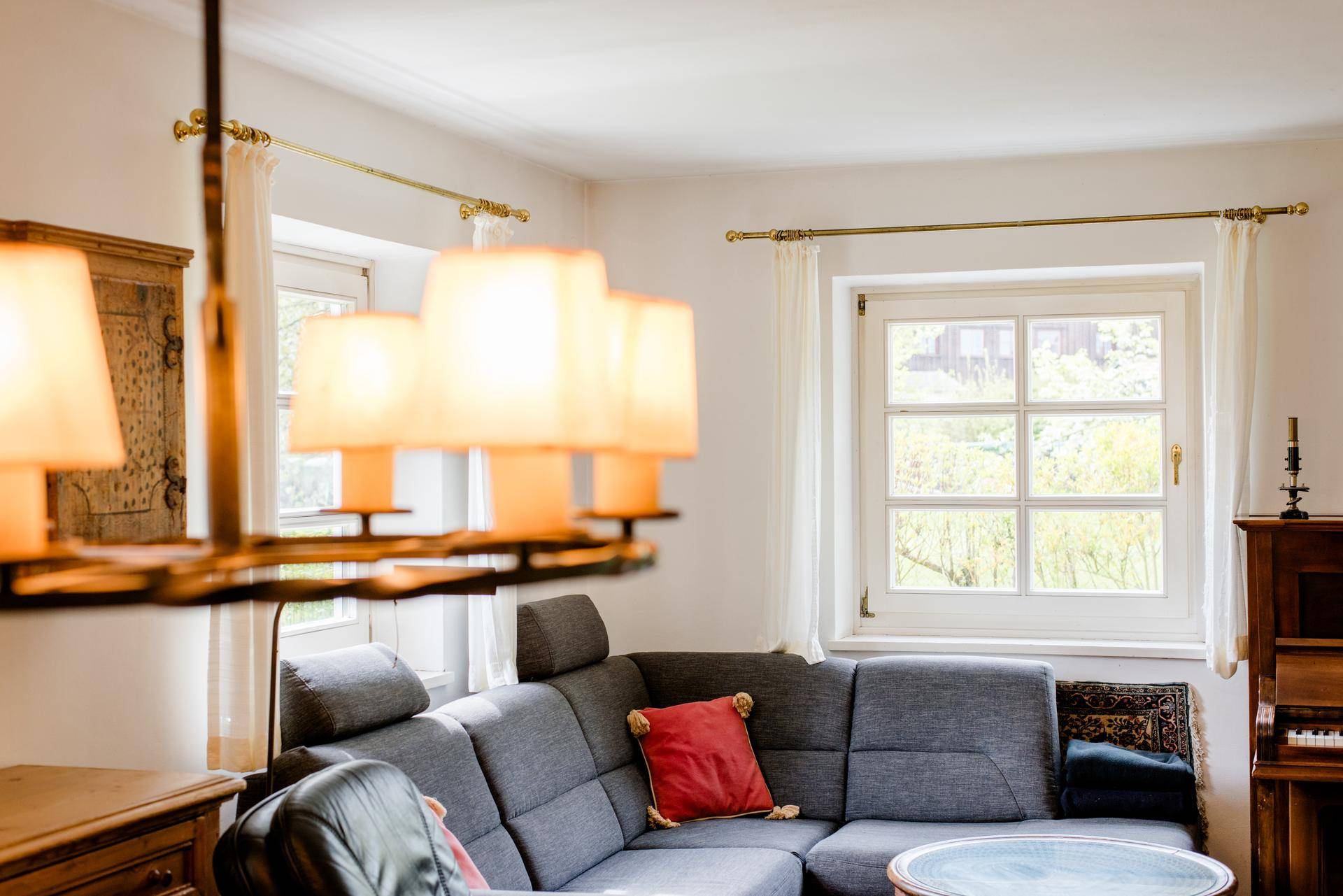 Gemütliches Wohnzimmer mit grauem Sofa, Holzboden und Fenstern mit Blick ins Grüne.