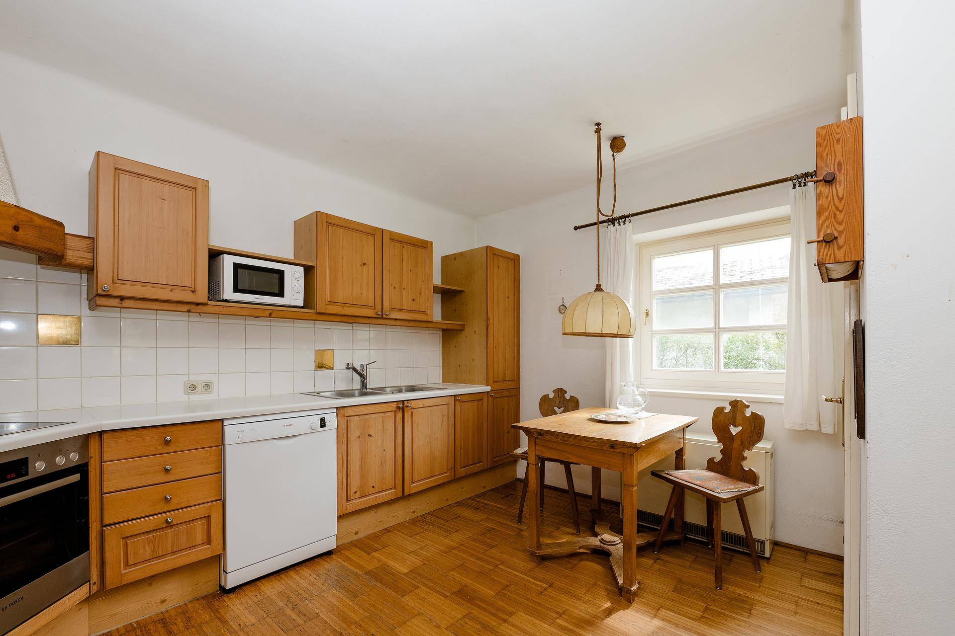 Traditionelle Küche mit Holzschränken, Einbaugeräten und einem kleinen Essbereich am Fenster.