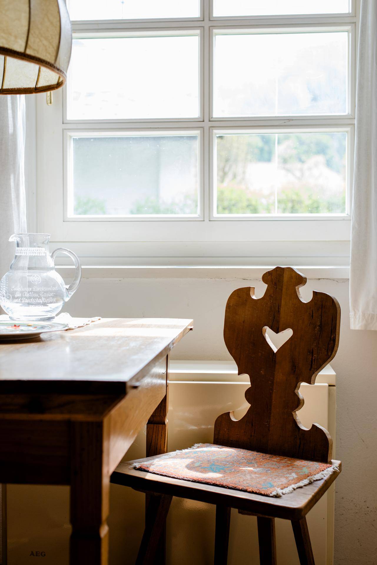 Detailaufnahme eines traditionellen Holzstuhls und Tisches am Fenster in einer Küche.