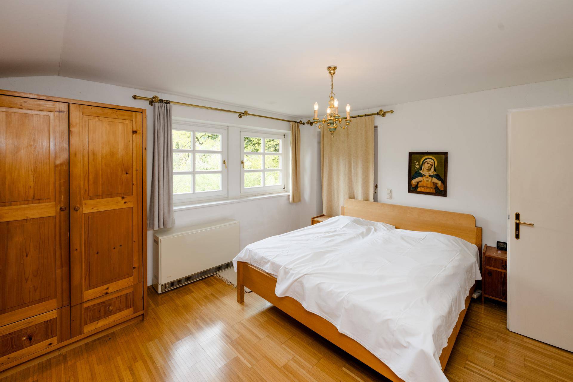Gemütliches Schlafzimmer mit Holzboden, Holzschrank und Fenster mit Blick ins Grüne.