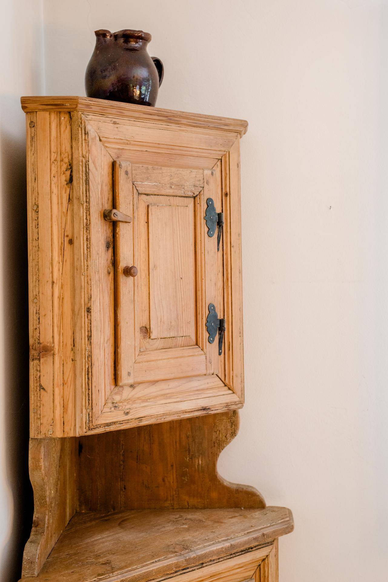 Detailaufnahme eines rustikalen Eckschranks aus Holz mit traditionellen Beschlägen.