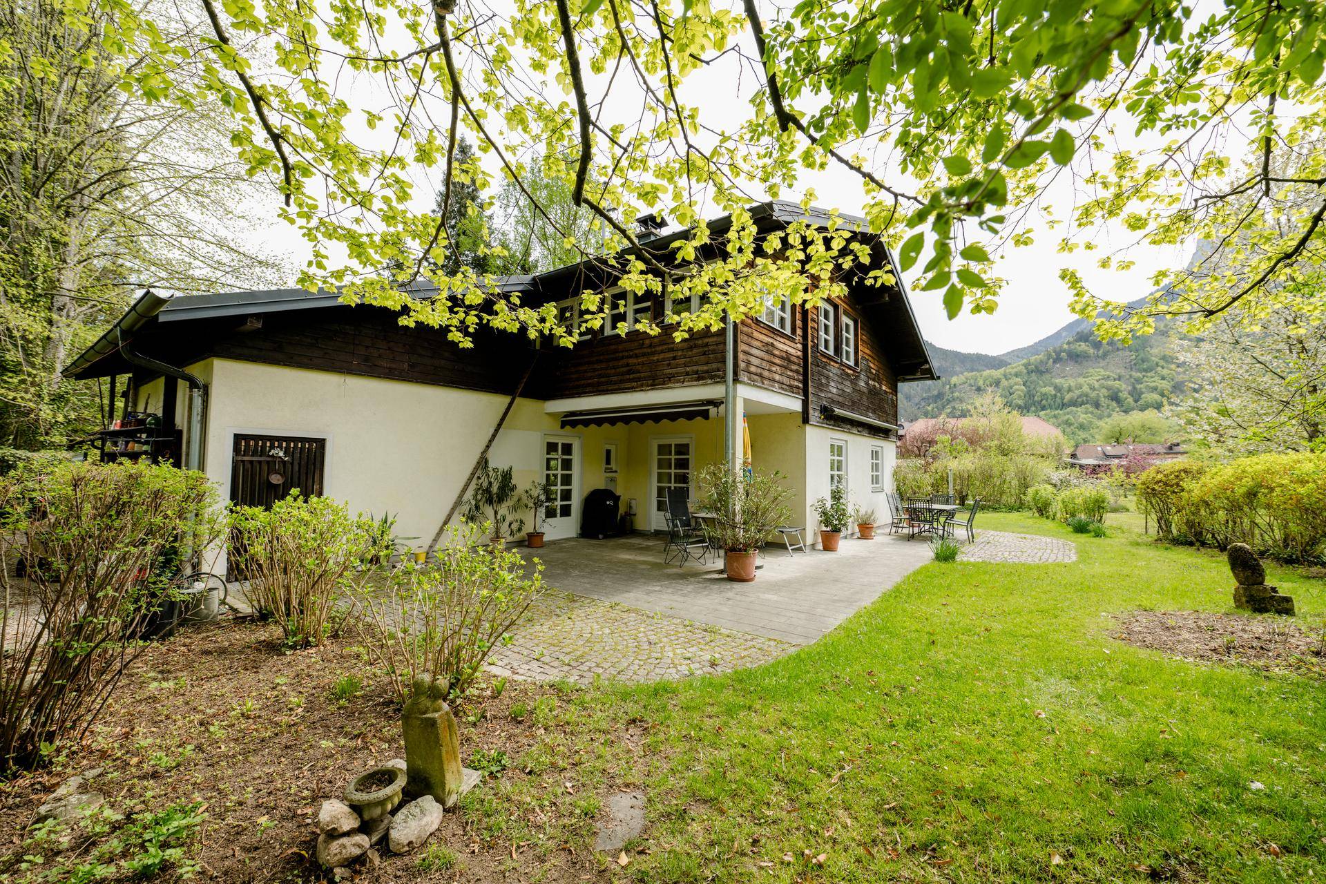 Großzügige gepflasterte Terrasse am Haus, umgeben von einem grünen Garten und Bäumen.