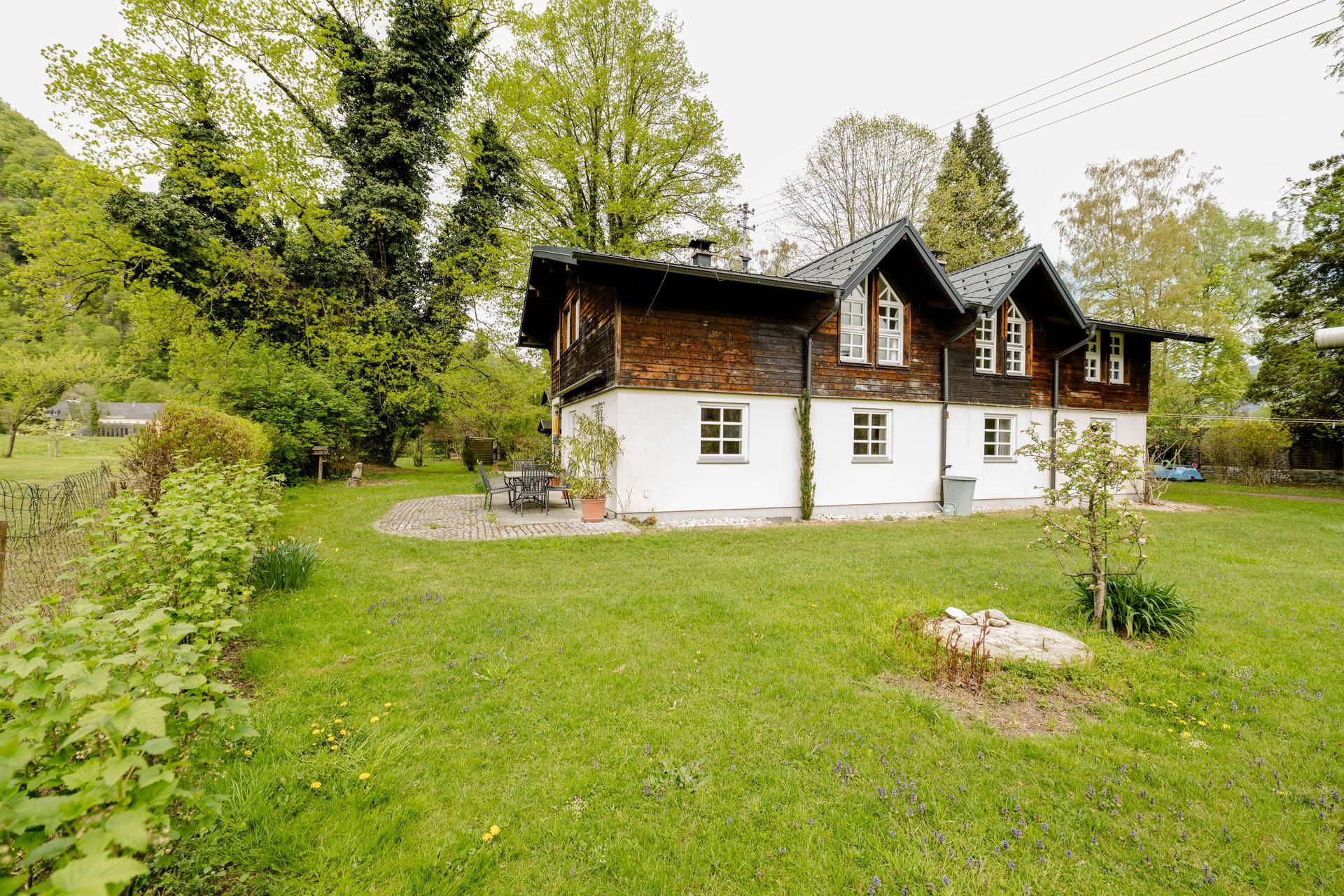 Seitenansicht des Hauses mit weitläufigem Garten, kleiner Terrasse und Blick auf die Berge.